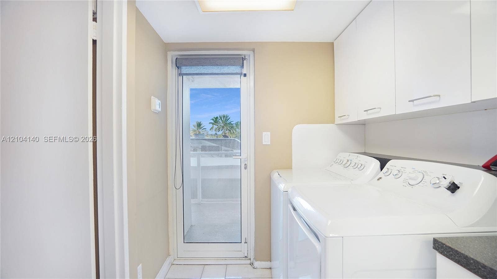 111 N Pompano Beach Boulevard, #304, Pompano Beach, FL 33062 Laundry space featuring white flat-panel upper cabinetry, tile flooring, and a glass-paneled exterior door