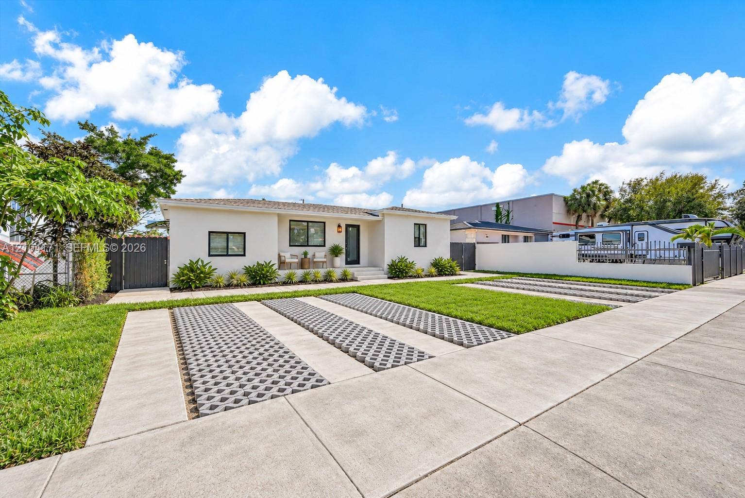 745 NW 32nd Avenue, Miami, FL 33125 Single-story exterior featuring a light-toned stucco facade, multi-vehicle parking pad with decorative concrete pavers, and perimeter fencing