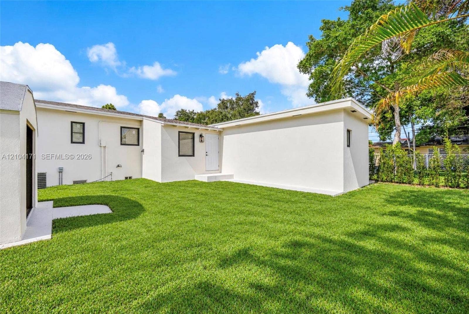 745 NW 32nd Avenue, Miami, FL 33125 Backyard featuring a manicured lawn, smooth stucco exterior, and mature perimeter trees