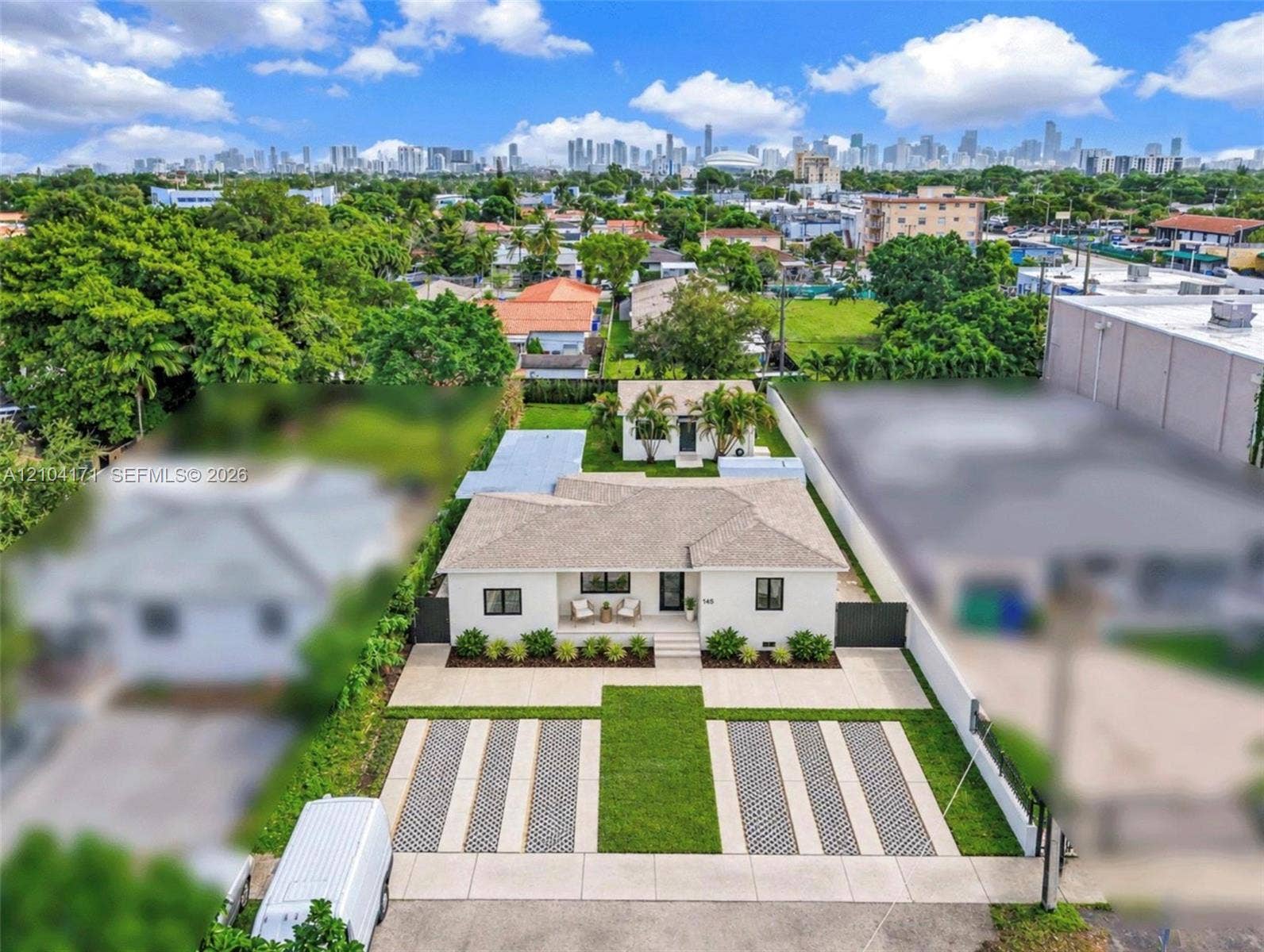 745 NW 32nd Avenue, Miami, FL 33125 Single-story residence featuring a hipped roof, paved multi-car driveway with integrated turf ribbons, enclosed yard with solid perimeter fencing, and a detached structure