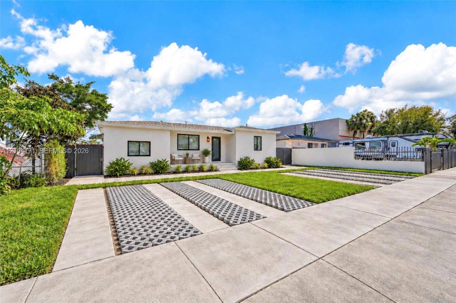 745 NW 32nd Avenue, Miami, FL 33125 Single-story exterior featuring light-toned stucco siding, concrete ribbon driveway with integrated permeable pavers, manicured lawn, and gated perimeter fencing