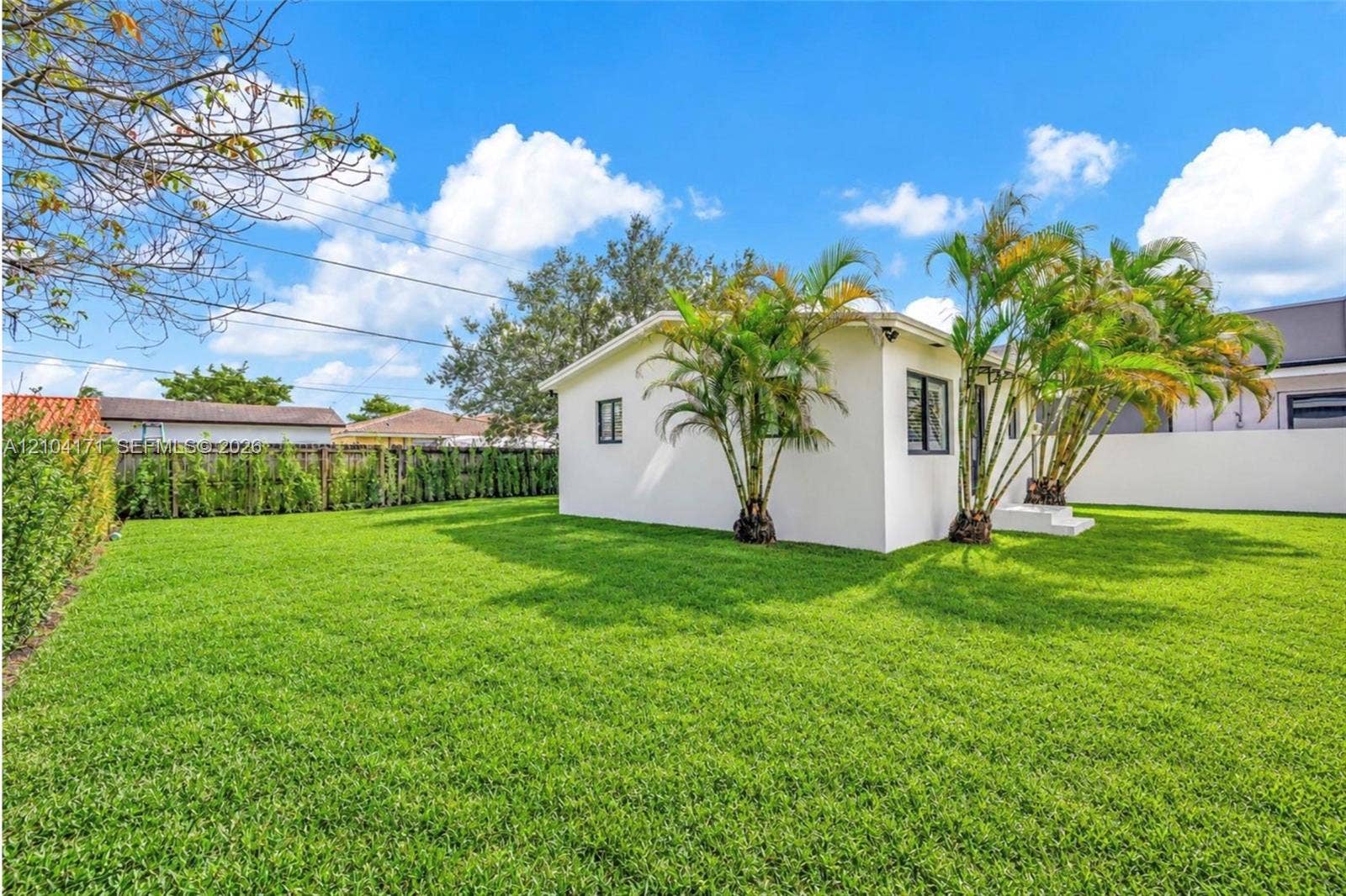 745 NW 32nd Avenue, Miami, FL 33125 Expansive backyard featuring a manicured lawn, established palm trees, hedge fencing, and a crisp white exterior finish