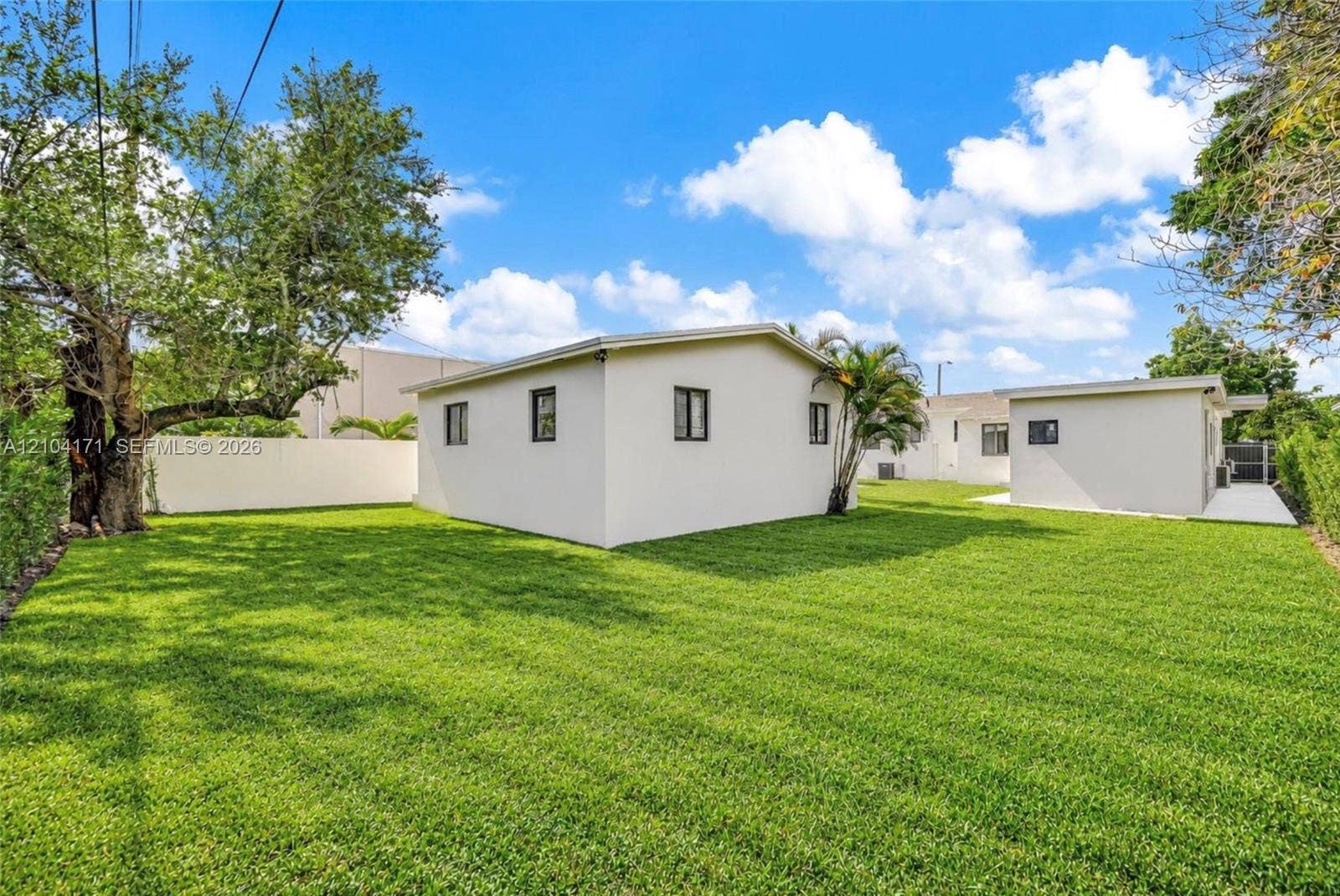 745 NW 32nd Avenue, Miami, FL 33125 Expansive backyard featuring a manicured lawn, perimeter masonry wall, mature trees, and detached structure