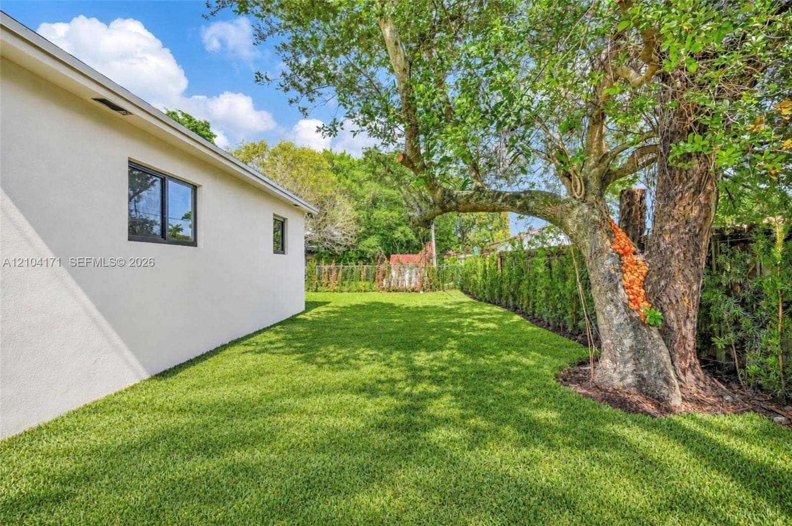 745 NW 32nd Avenue, Miami, FL 33125 Side yard featuring a smooth stucco exterior, expansive lawn, mature tree, and perimeter privacy hedges