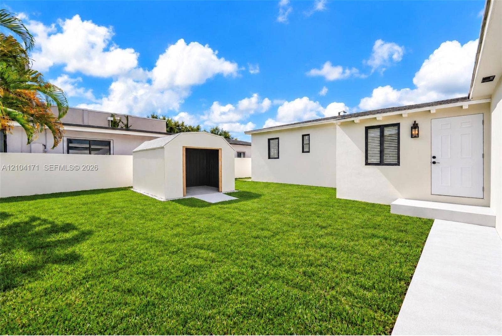 745 NW 32nd Avenue, Miami, FL 33125 Backyard featuring a manicured lawn, perimeter masonry wall, detached storage shed, and concrete walkway