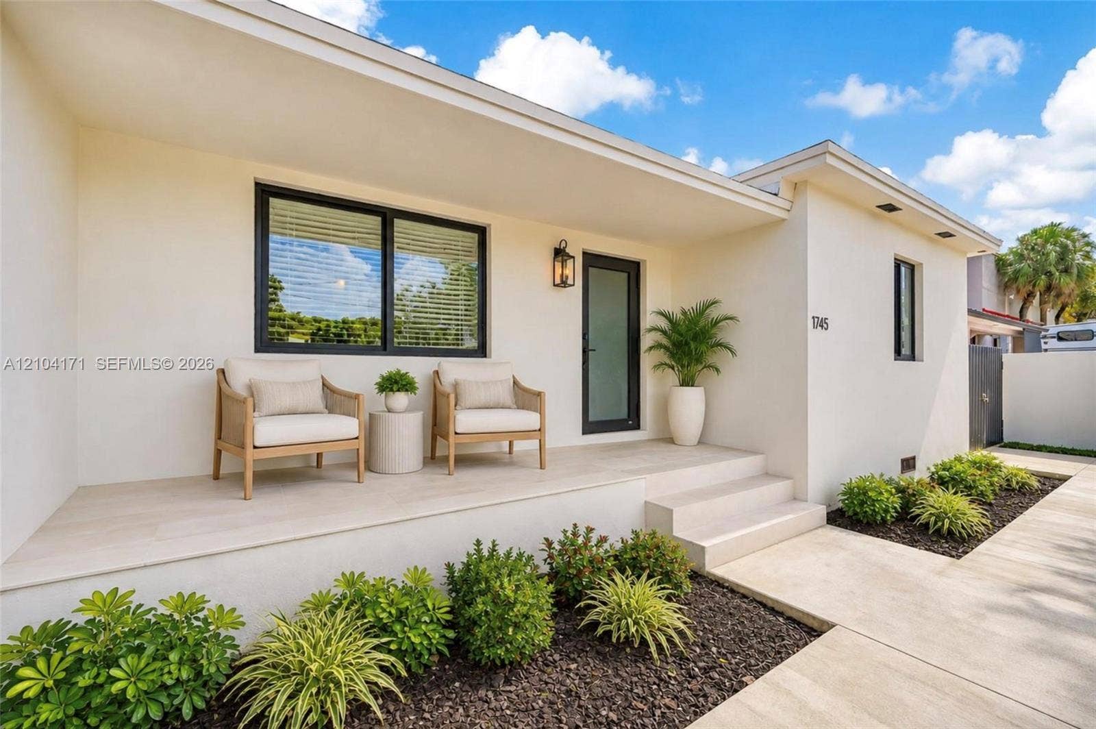 745 NW 32nd Avenue, Miami, FL 33125 Stucco exterior featuring an expansive covered porch, tiled flooring, dark-framed windows, and a glass-panel entry door
