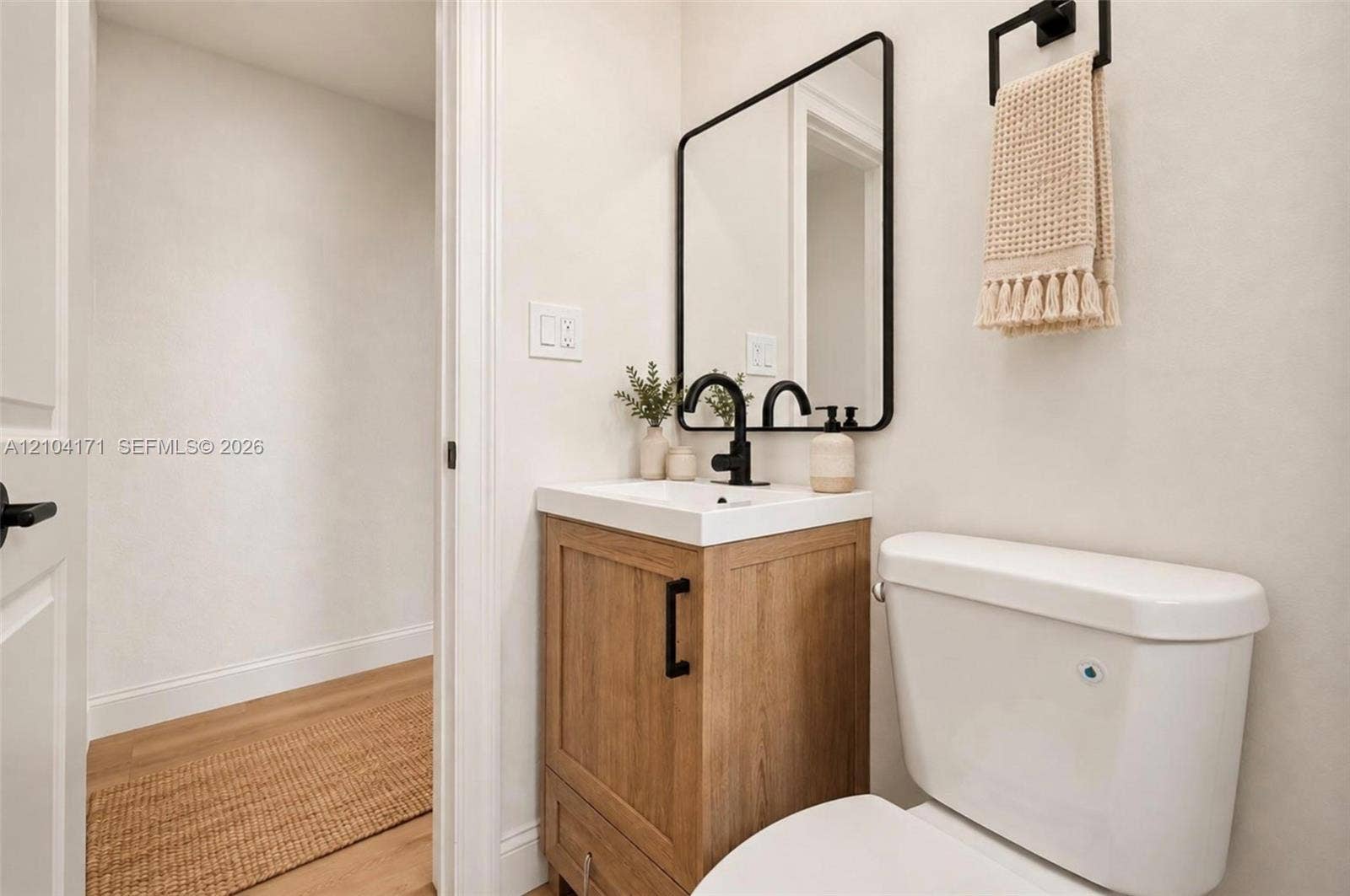 745 NW 32nd Avenue, Miami, FL 33125 Wood-finish vanity with a rectangular sink, matte black faucet, wall-mounted rectangular mirror with a black frame, and a coordinating matte black towel ring
