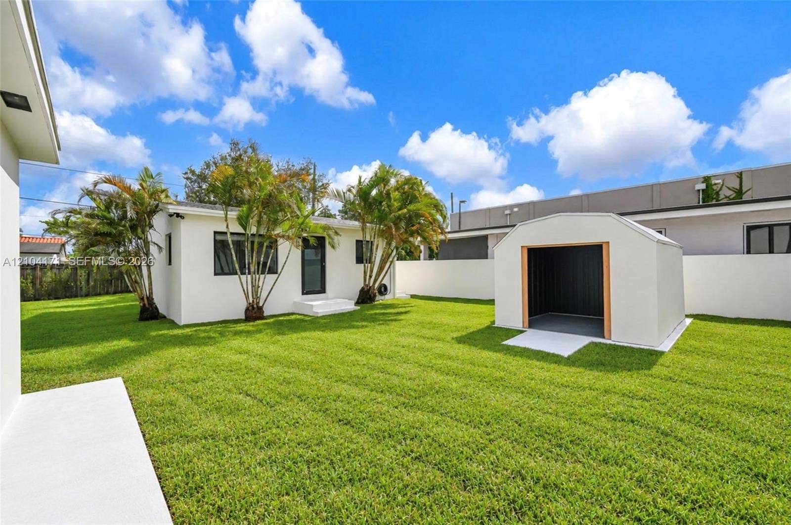 745 NW 32nd Avenue, Miami, FL 33125 Expansive backyard featuring a manicured lawn, white perimeter wall, detached storage shed, and mature palm trees