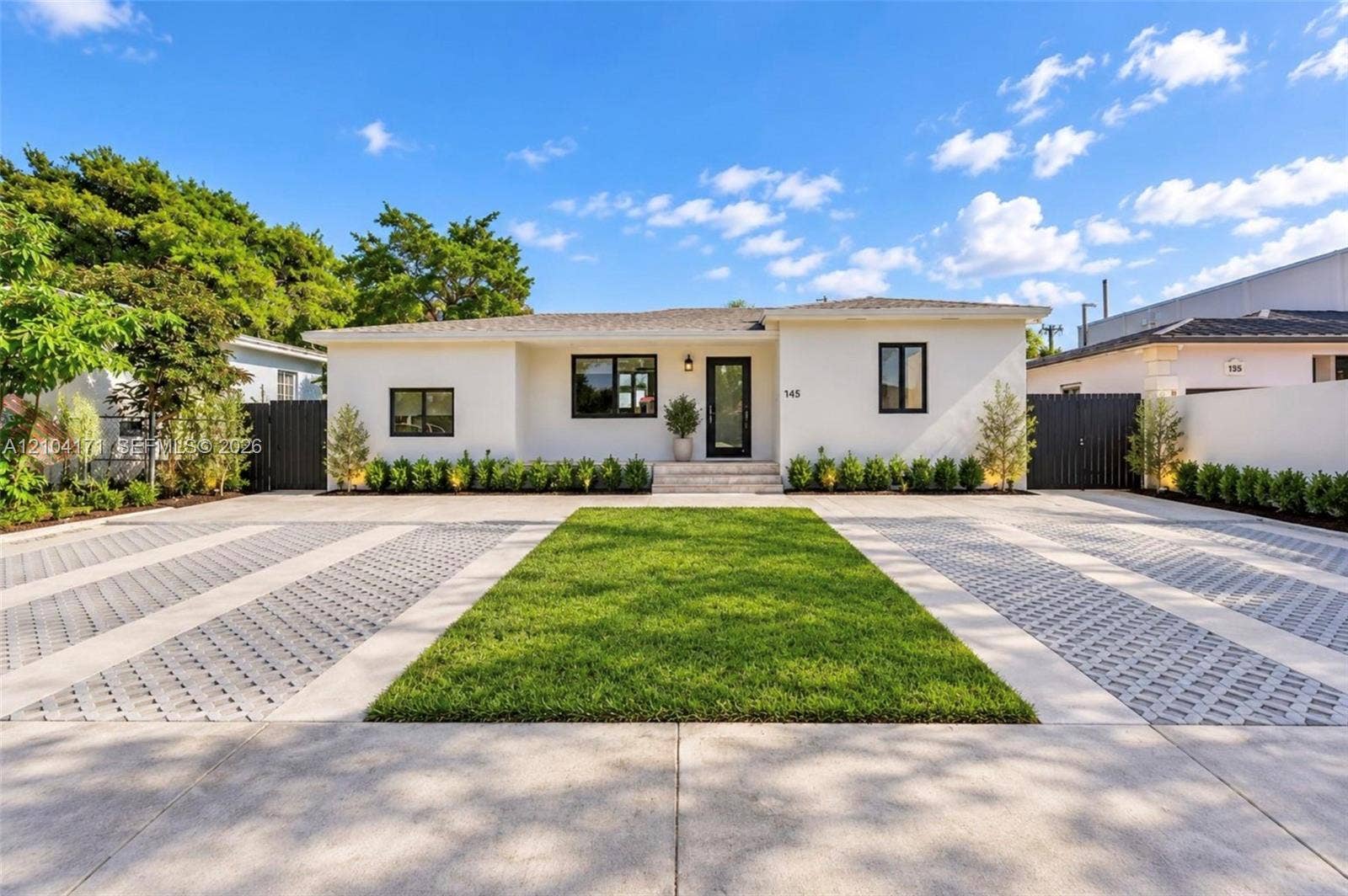 745 NW 32nd Avenue, Miami, FL 33125 Single-story residence featuring a smooth stucco facade, contrast-trimmed windows, a central entryway with stone steps, and an expansive paved motor court with integrated turf landscaping