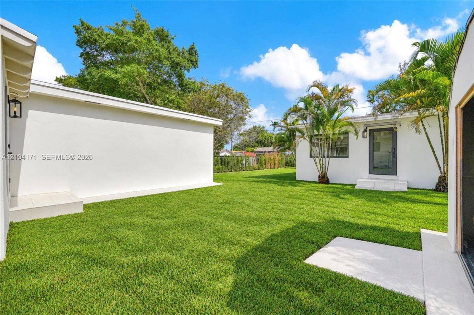 745 NW 32nd Avenue, Miami, FL 33125 Expansive backyard featuring a manicured lawn, concrete patio surfaces, and mature palm trees