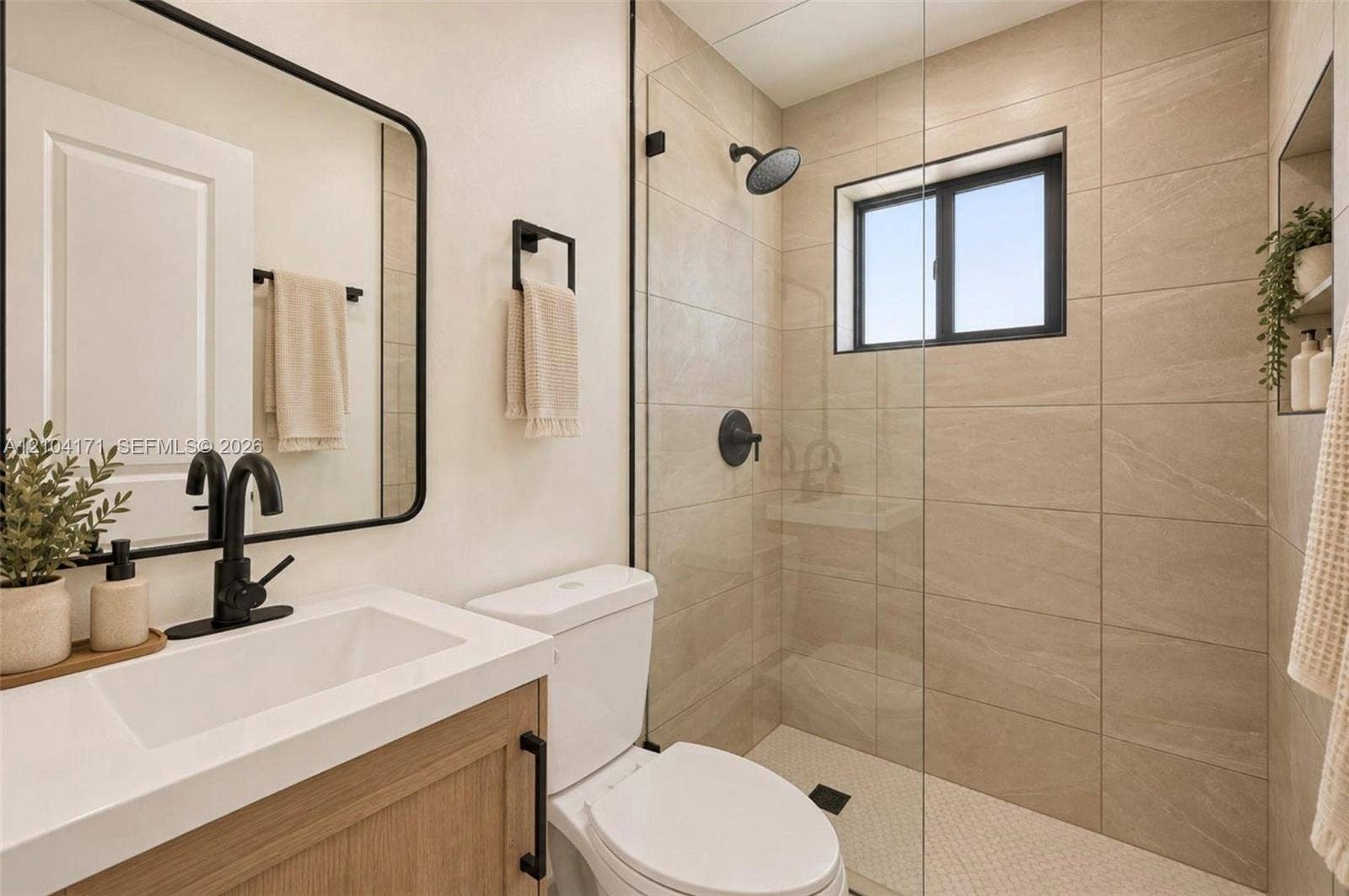 745 NW 32nd Avenue, Miami, FL 33125 Bathroom featuring a wood-finish vanity with a white countertop, matte black hardware, a glass-enclosed shower with large-format tile surround, and a built-in shower niche