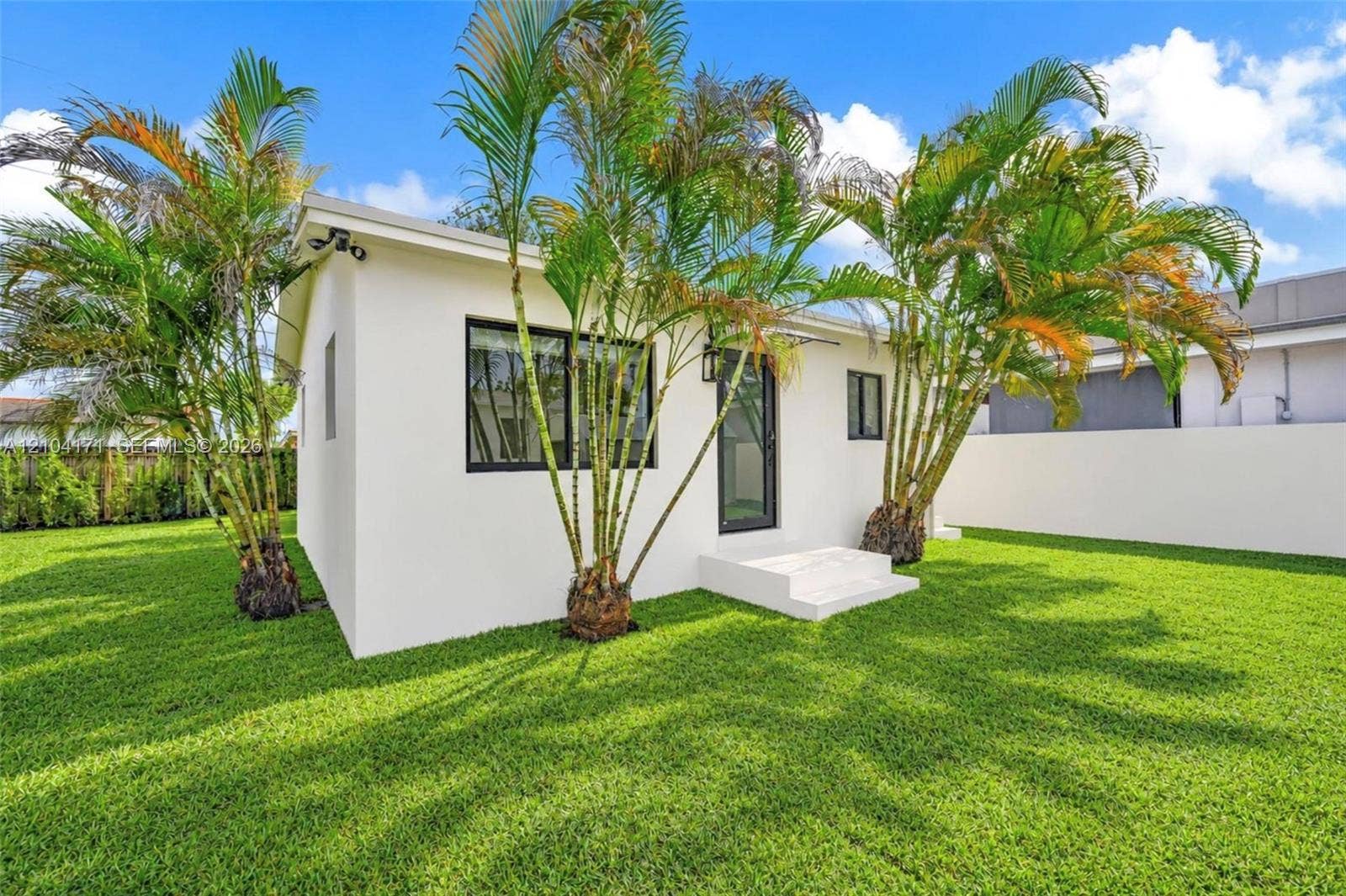 745 NW 32nd Avenue, Miami, FL 33125 Exterior of white stucco structure featuring dark-framed windows, a glass-panel door, concrete stairs, and perimeter privacy wall