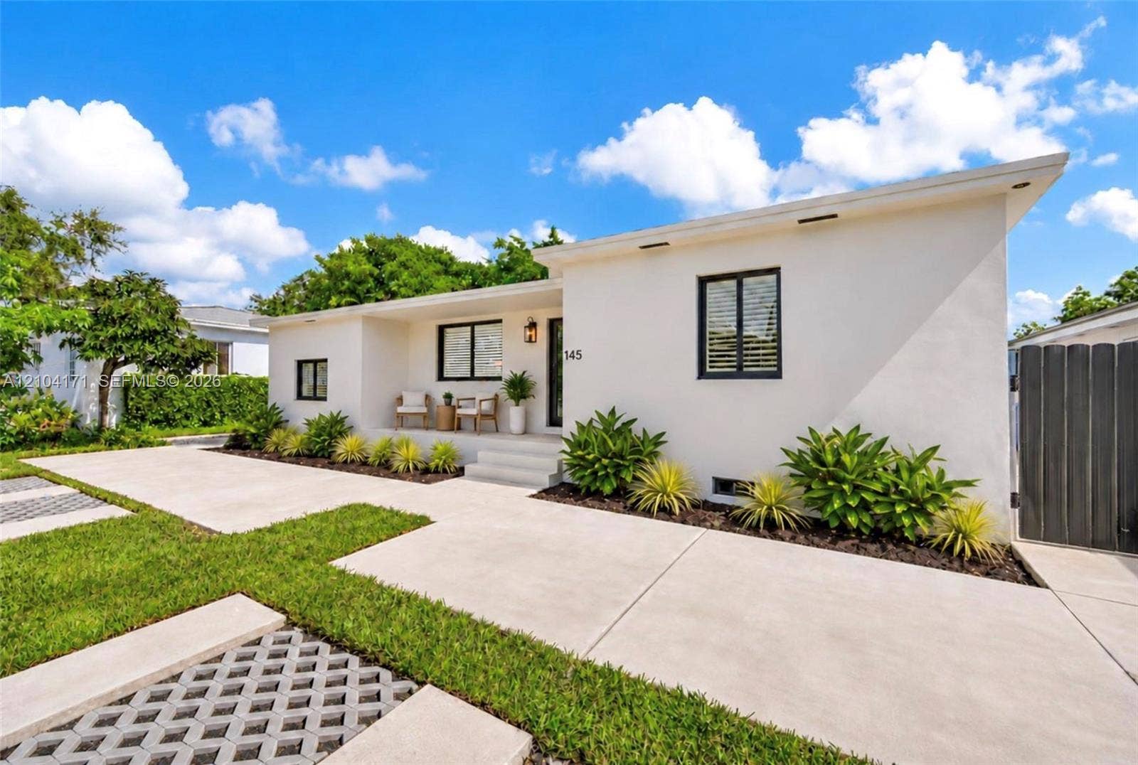 745 NW 32nd Avenue, Miami, FL 33125 Single-story residence featuring a smooth stucco exterior, a concrete driveway, integrated recessed exterior lighting, black-framed windows, and a landscaped front garden with paver-accented lawn