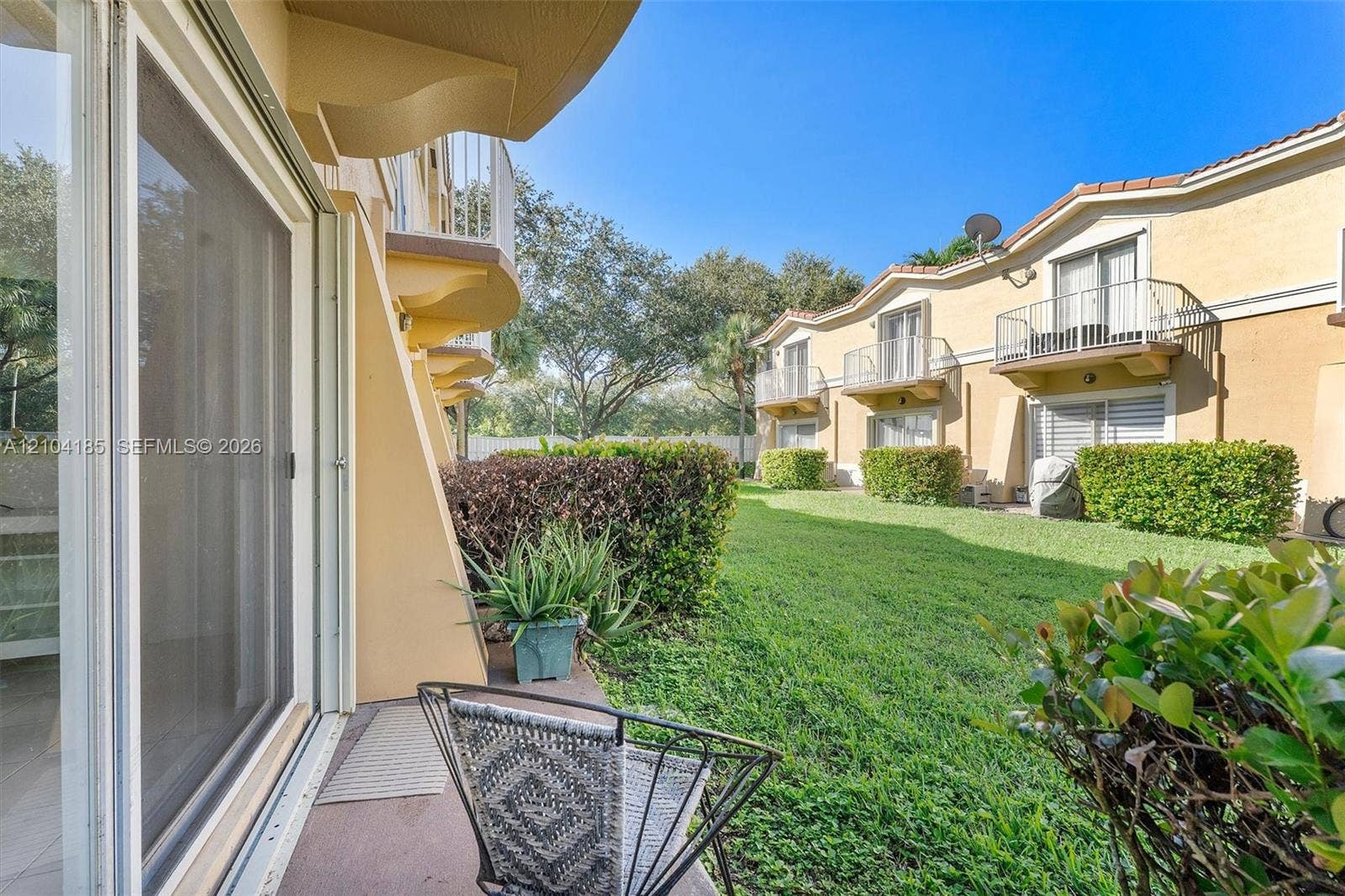 Ground-level patio with sliding glass door entry, manicured green space, and private metal balconies