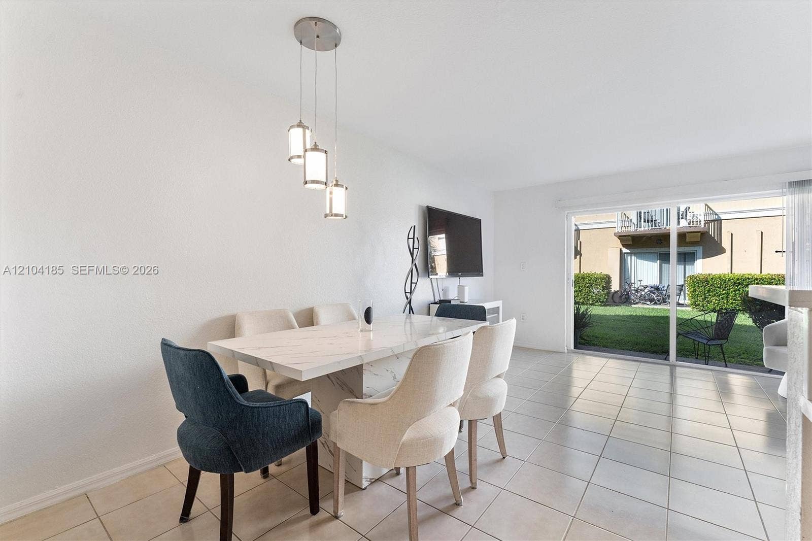 Neutral tile flooring, multi-light pendant fixture, and sliding glass doors with access to an exterior green space