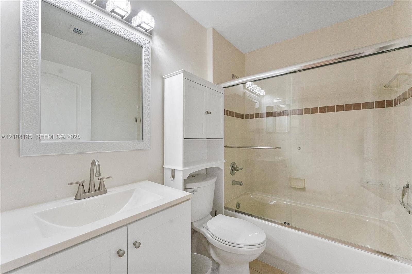 Bathroom featuring a vanity with an integrated sink, built-in over-the-toilet storage cabinet, framed wall mirror, and a tub-shower combination with sliding glass doors