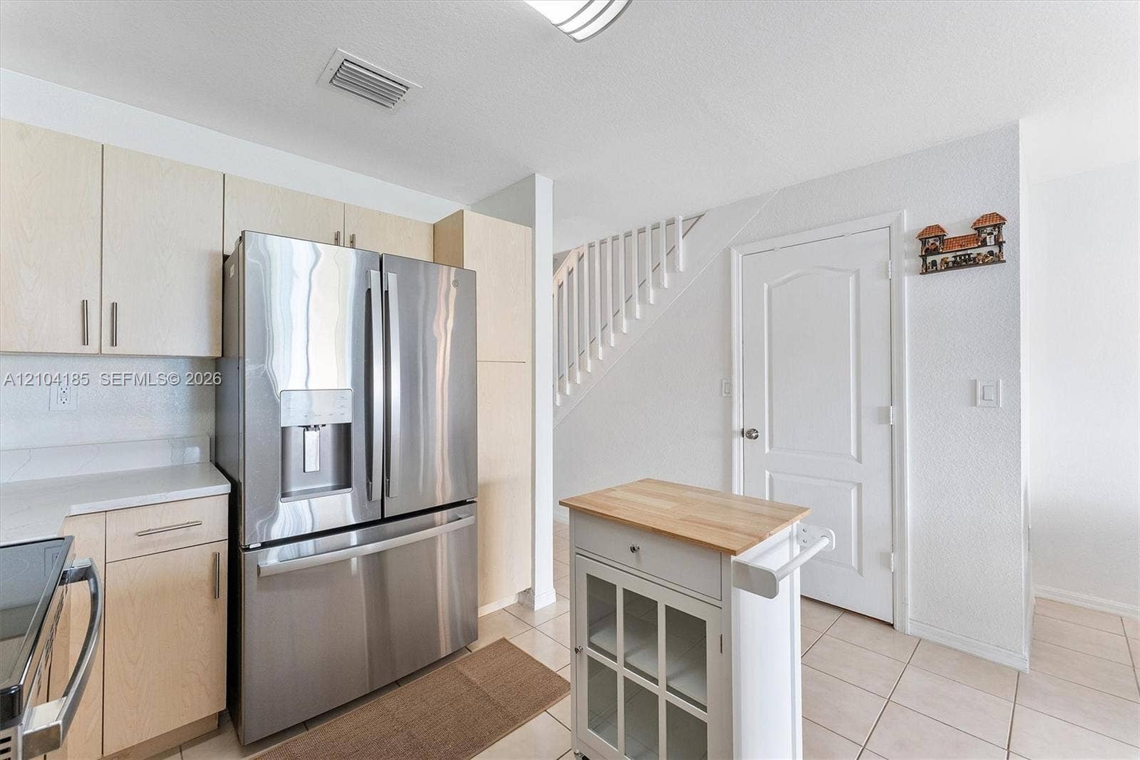 Kitchen featuring light-finish cabinetry, stainless steel refrigerator, white solid-surface countertops, and tiled flooring