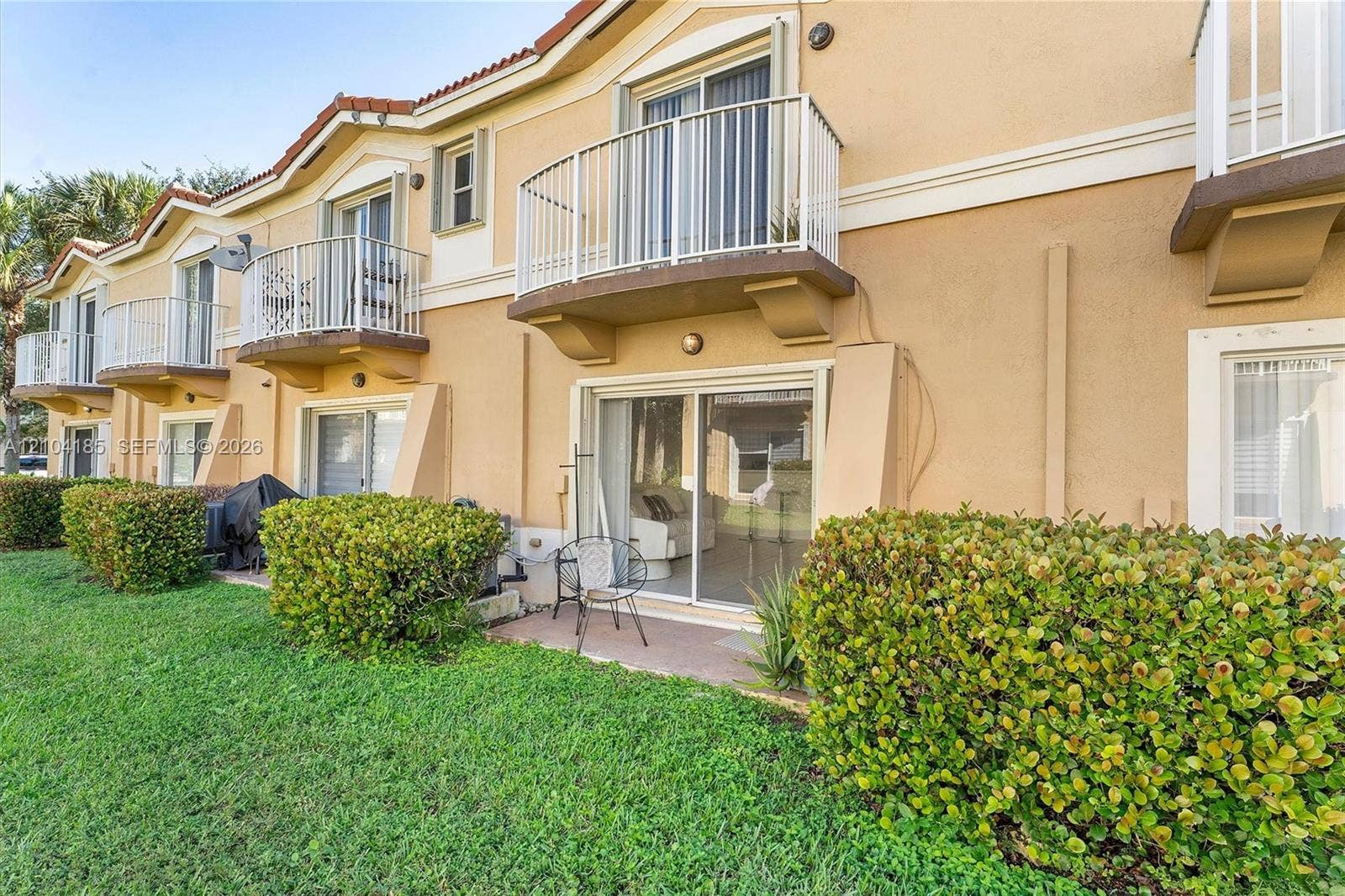 Stucco exterior featuring multiple private balconies with white metal railings, sliding glass doors, and a ground-level patio area