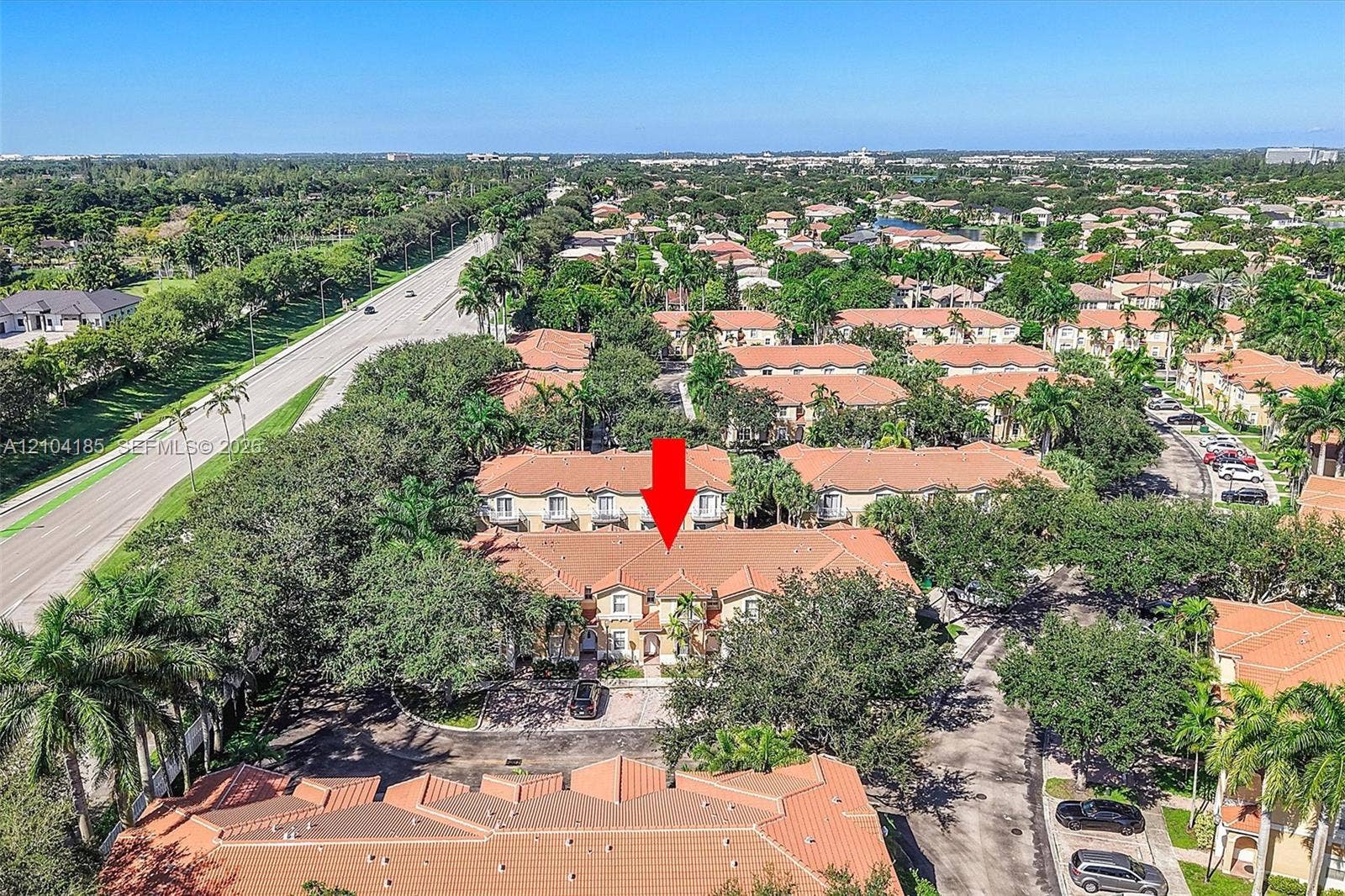 Aerial perspective of multi-story townhome featuring a terracotta-tiled roof, light-toned stucco exterior, and balconies with decorative metal railings, situated within a landscape of mature trees