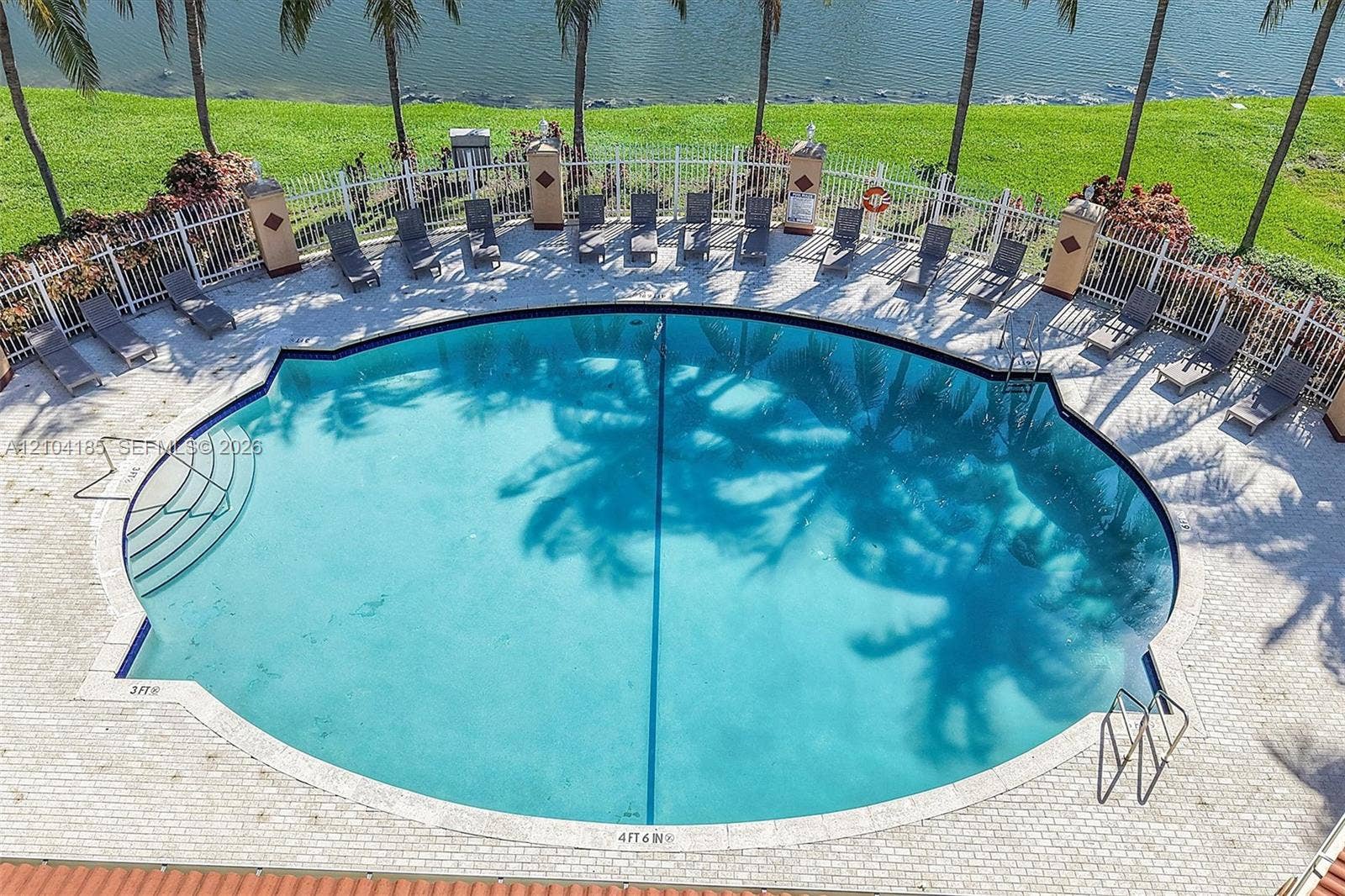Circular swimming pool featuring built-in steps, a perimeter masonry deck, decorative pillars, and a metal enclosure