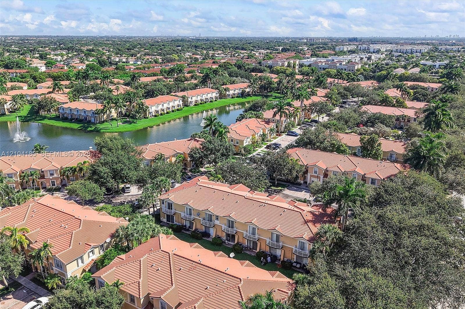 Aerial perspective of a multi-unit complex featuring tile roofing, stucco exteriors, balcony railings, water-centered hardscaping, and mature landscaping