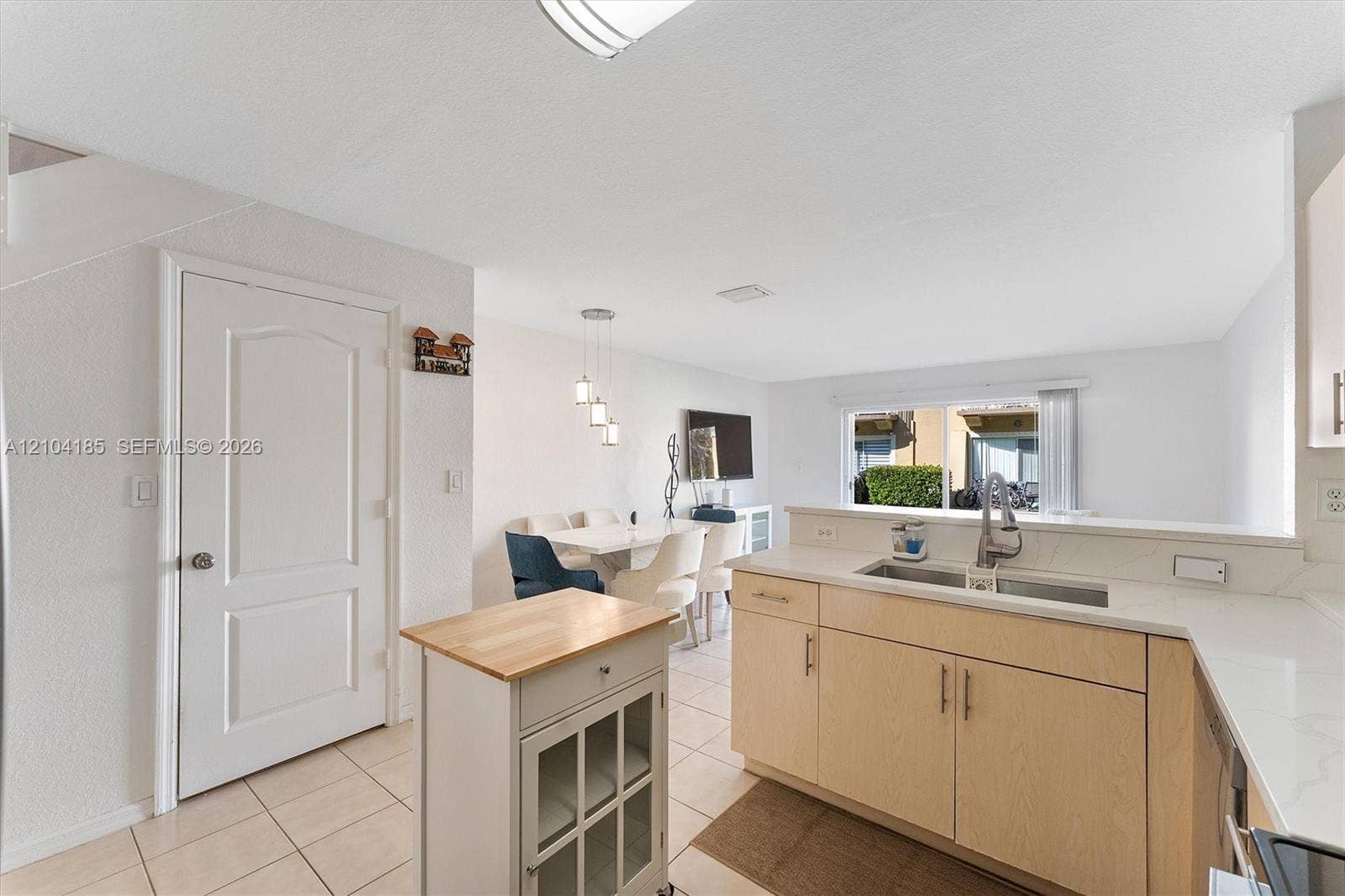Kitchen featuring light wood-finish cabinetry, solid-surface countertops, dual-basin stainless steel sink, and tile flooring