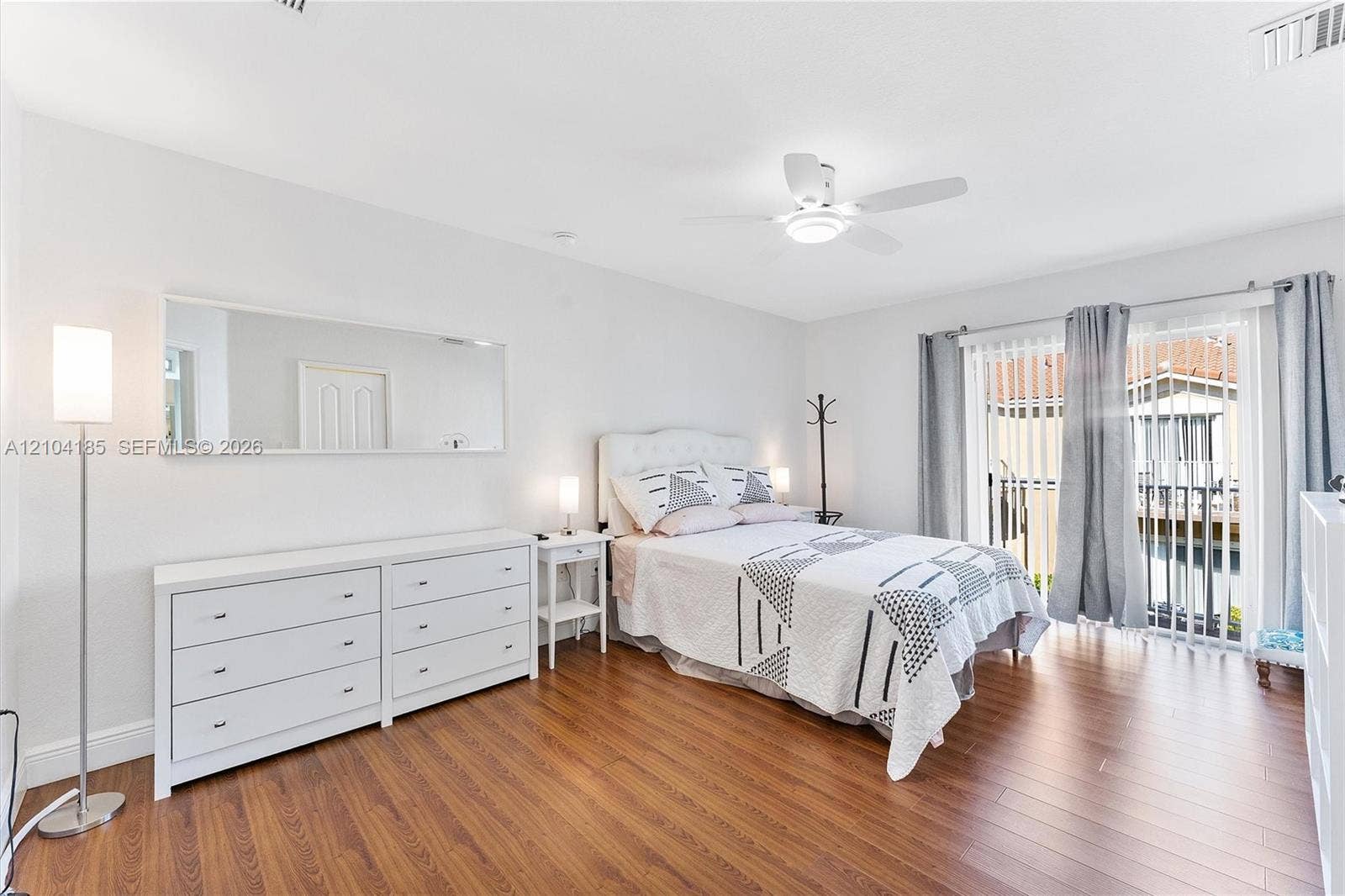 Wood-finish flooring, ceiling fan with integrated lighting, expansive wall-mounted mirror, and sliding glass patio door