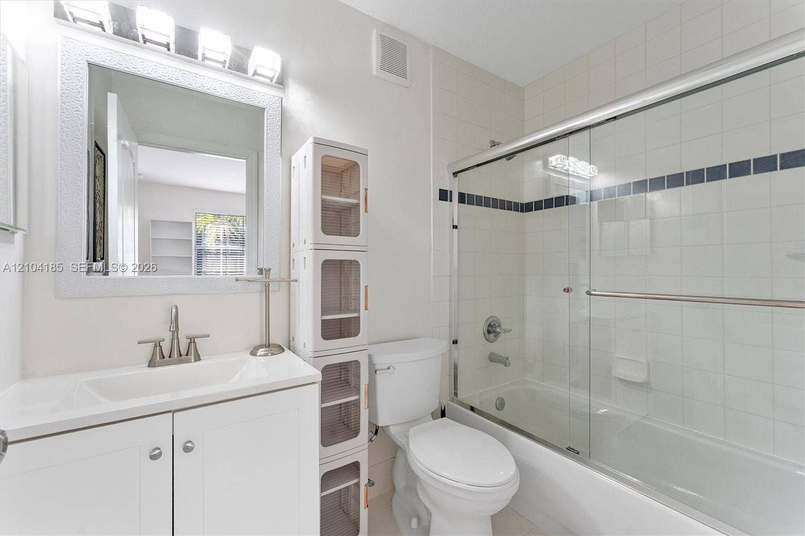 Bathroom featuring a white vanity cabinet with an integrated basin, a framed wall mirror, a multi-light fixture, and a combination shower and tub enclosure with sliding glass doors and tiled walls