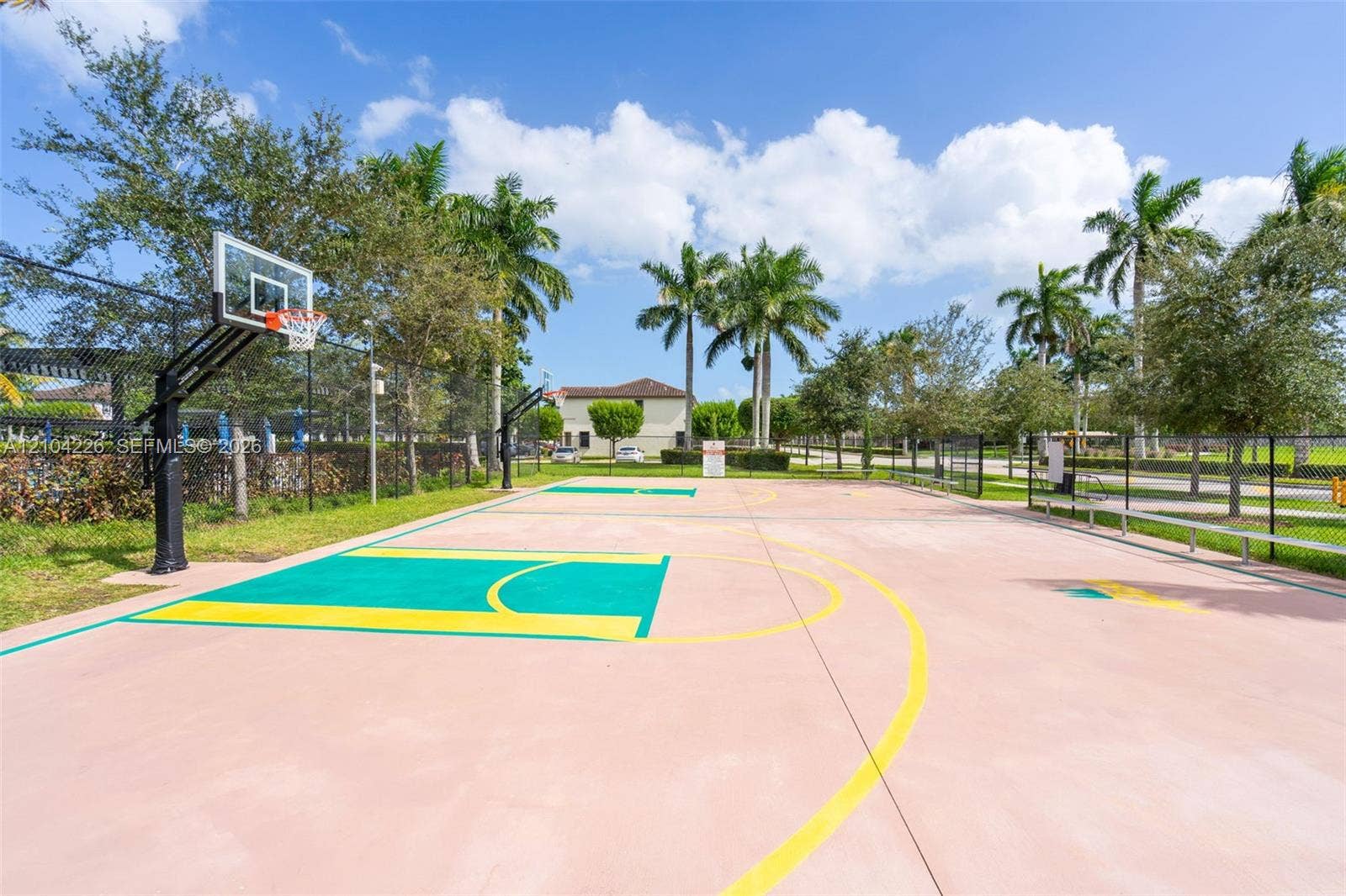 11555 SW 248th Lane, Homestead, FL 33032 Outdoor basketball court with a multi-colored paved surface, steel hoops, and perimeter chain-link fencing, surrounded by mature palm trees and manicured landscaping