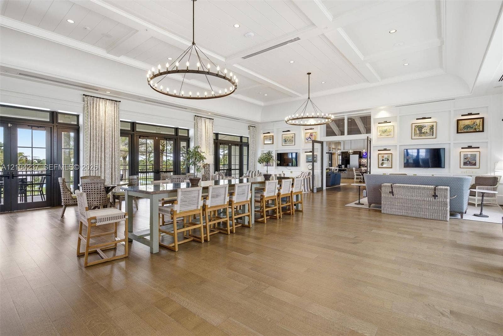 Spacious interior featuring coffered ceilings, wood-finish flooring, dual iron-frame wagon wheel chandeliers, and extensive built-in wall cabinetry