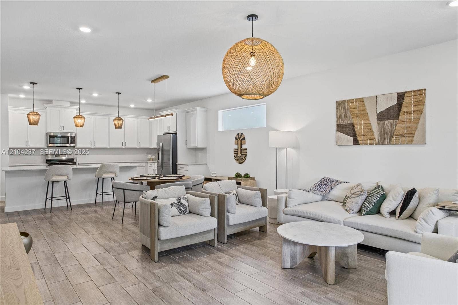Open-concept kitchen featuring white shaker-style cabinetry, stainless steel appliances, a kitchen island with bar seating, recessed lighting, and wood-finish tile flooring