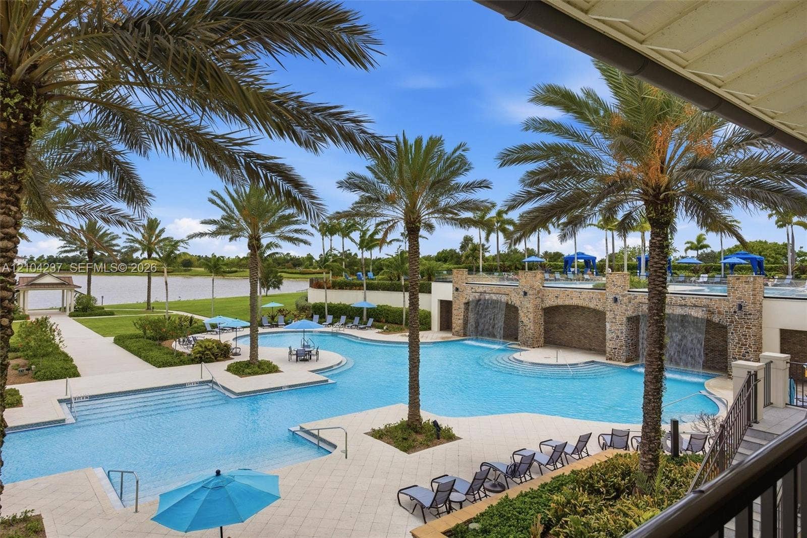 Resort-style pool featuring stone water features, tiered levels, stone-tiled decking, and mature palm landscaping