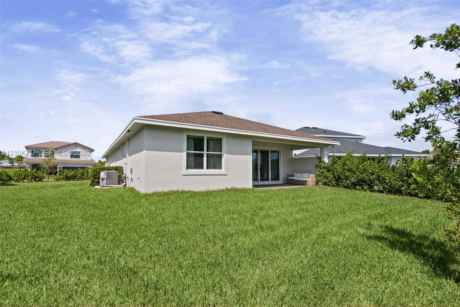 Stucco exterior with a hip roof, covered rear patio, sliding glass doors, and expansive lawn