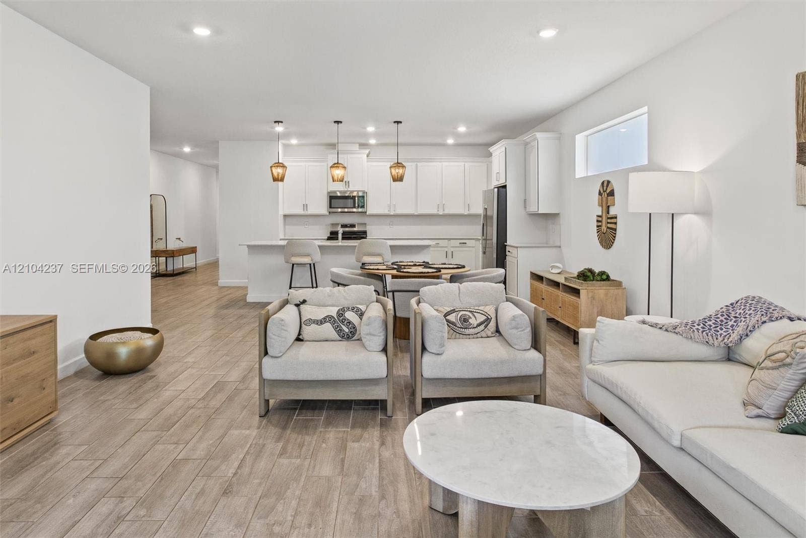 Open-concept area featuring wood-finish flooring, recessed lighting, and a kitchen equipped with white cabinetry, a center island, and triple pendant light fixtures
