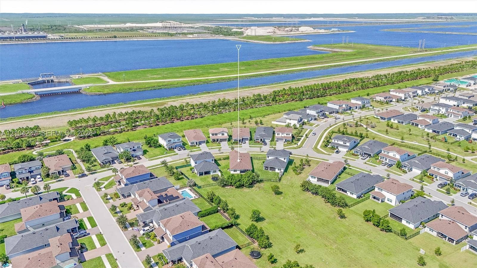 Aerial perspective showcasing a residential lot with a paved driveway, shingled roofing, and grass-covered grounds, situated in a suburban community near a waterway