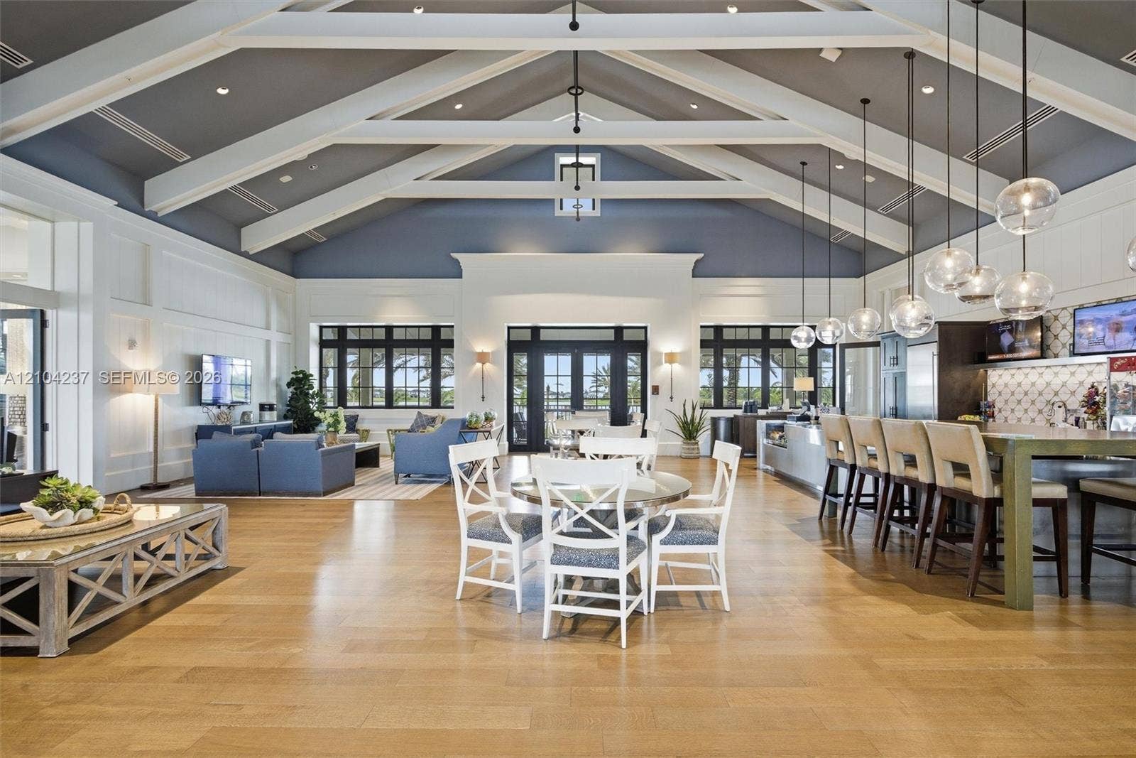 Vaulted ceiling with exposed white beams, wood-finish flooring, built-in bar area with stone-tile backsplash, and glass globe pendant lighting