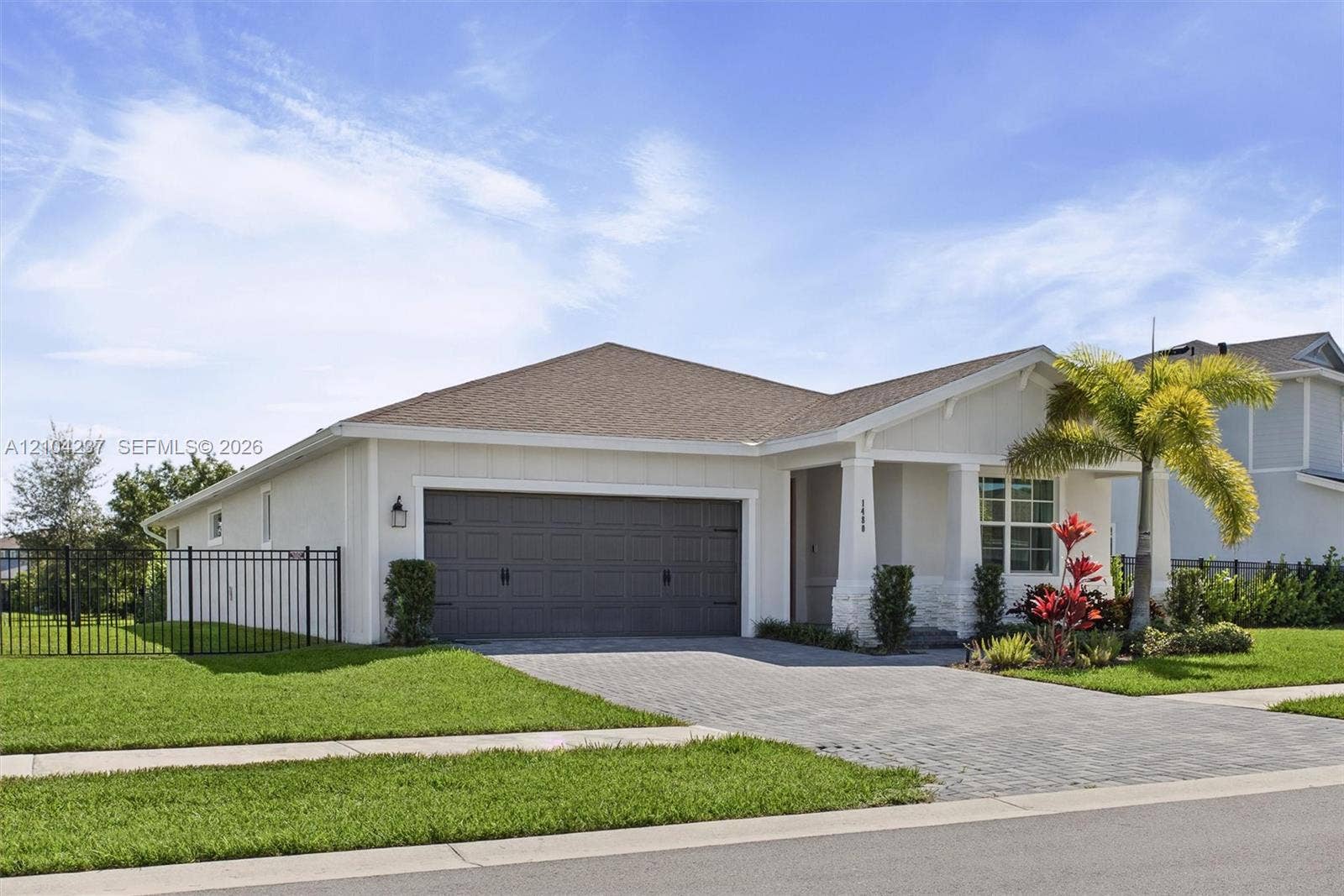 Single-story exterior featuring a light-toned facade, decorative stone accents, a two-car garage, and a paved driveway, complemented by manicured landscaping and a perimeter metal fence