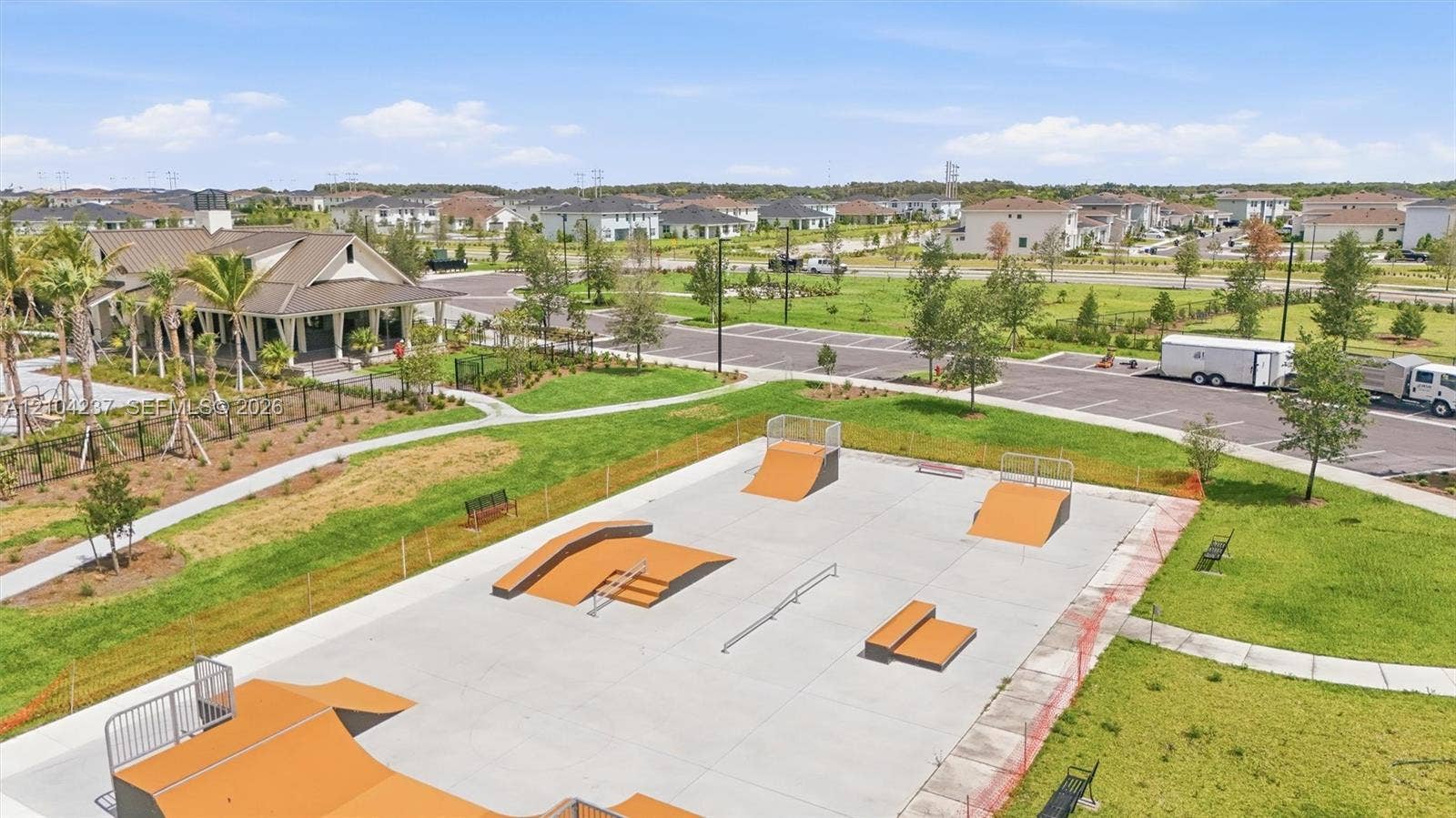 Concrete skate park featuring multiple ramps, grind rails, and a paved surface, set within a landscaped recreation area