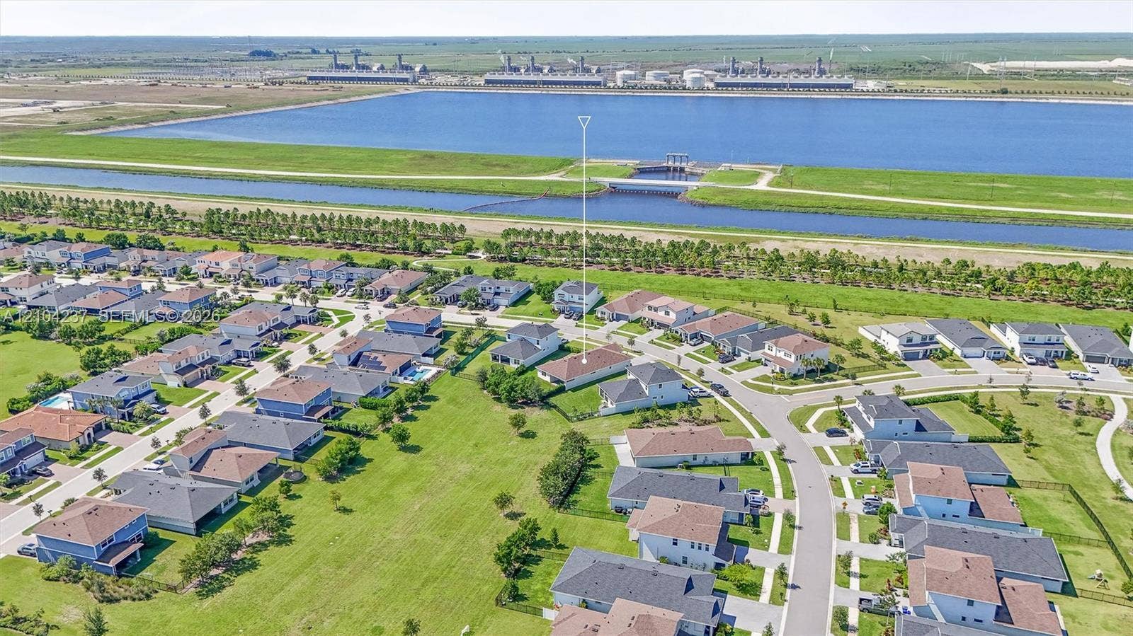 Aerial perspective of a residential property situated in a planned community, featuring a shingled roof, paved streets, and expansive green space