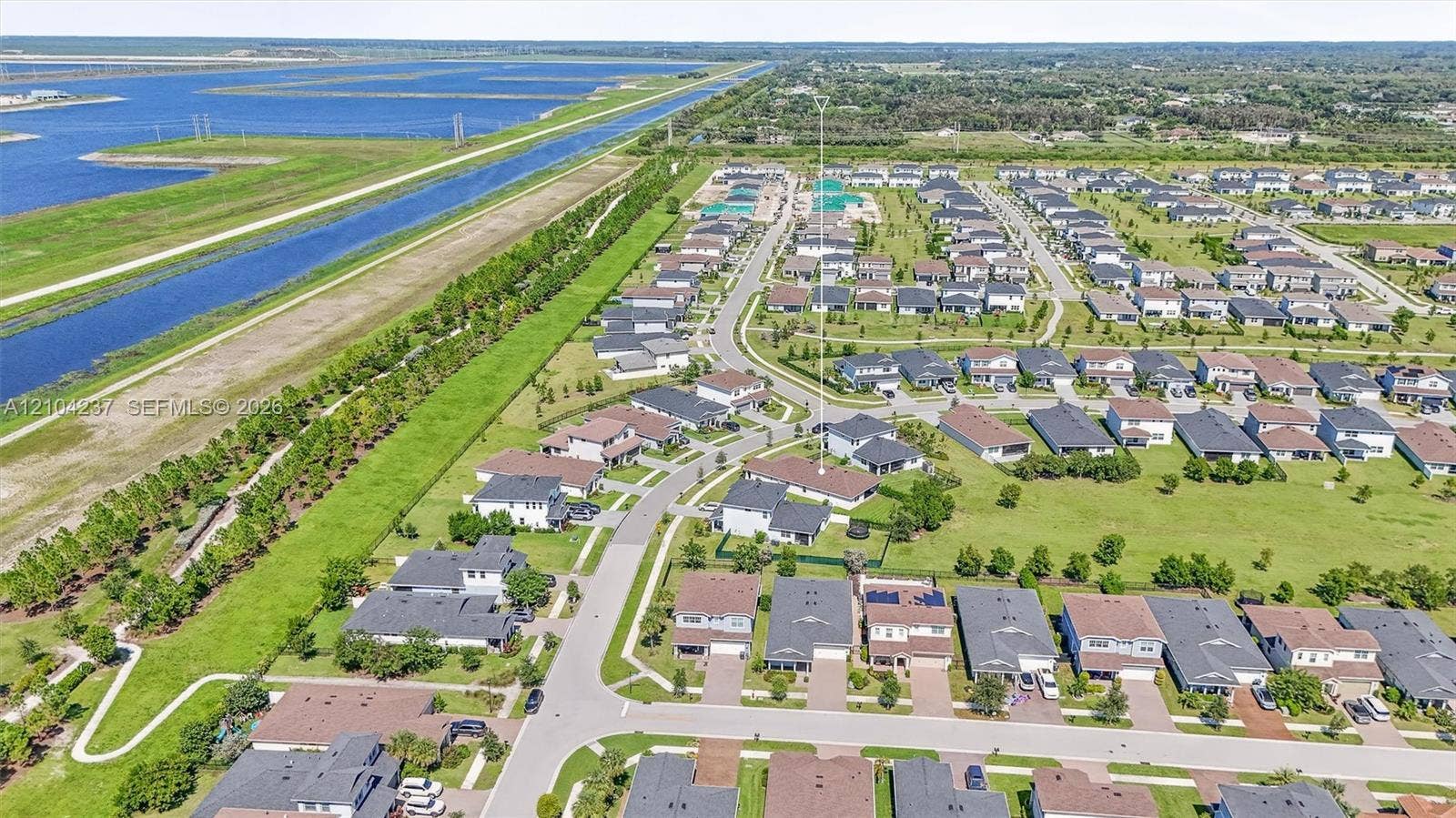 Aerial perspective of a residential community featuring paved roadways, concrete driveways, manicured lawns, and proximity to expansive waterway features