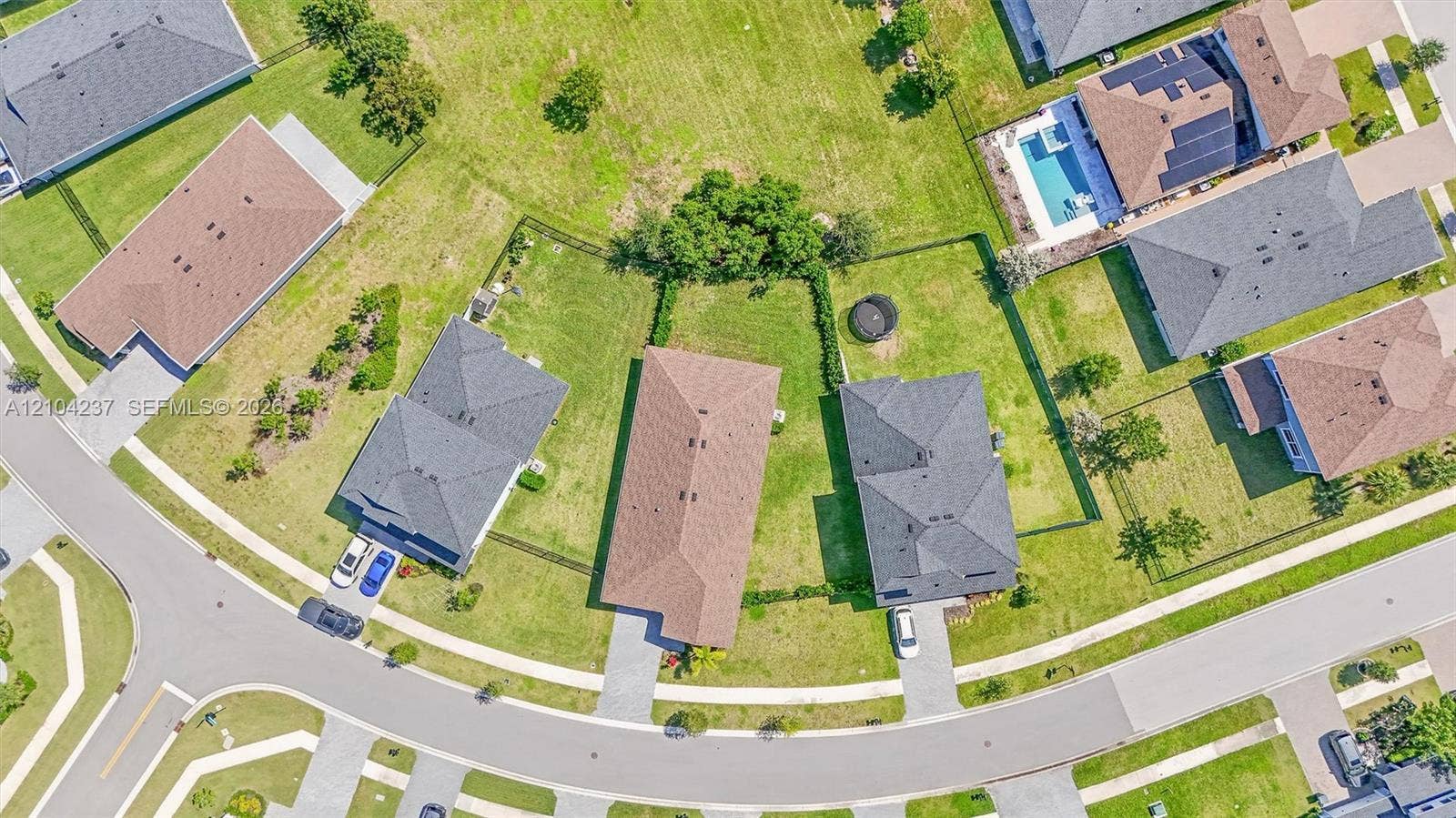 Aerial perspective of a residential property featuring a paved driveway, a multi-hip roofline, and a fenced-in grassy backyard