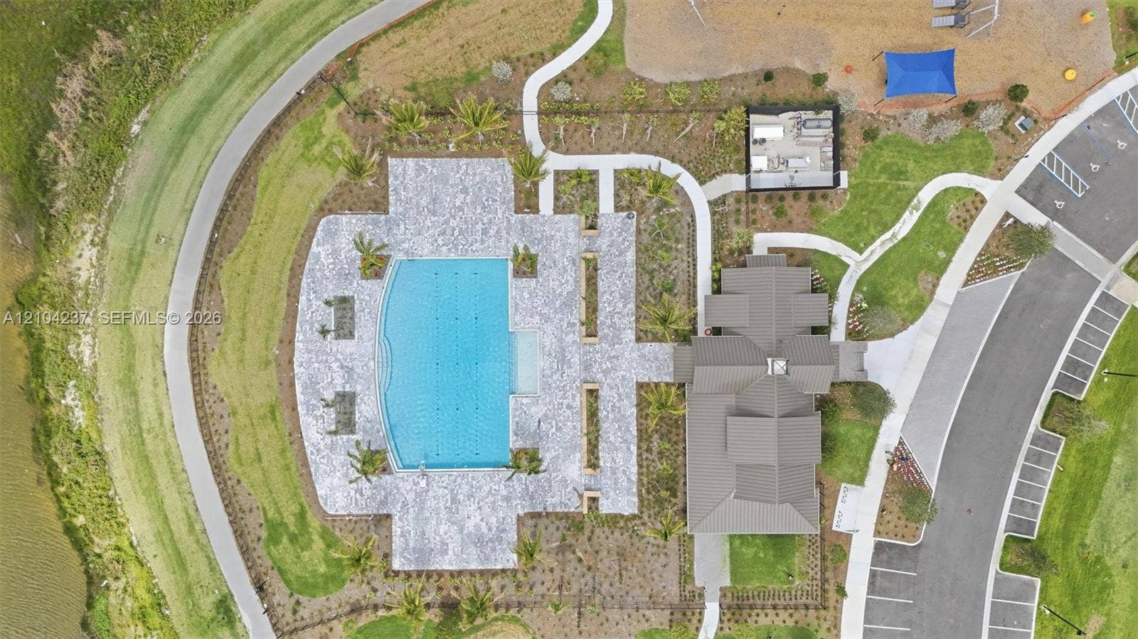 Aerial perspective of a community facility featuring a swimming pool, stone-paver pool deck, structured landscaping, and paved walking paths