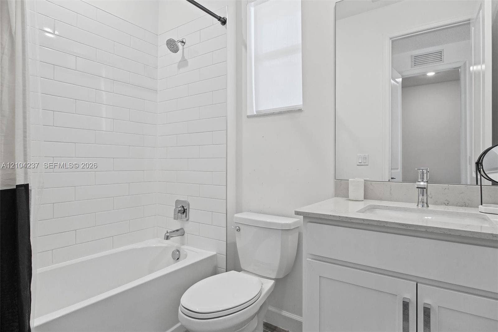 Bathroom featuring a white vanity with a composite countertop, undermount sink, subway tile shower surround, and a large wall-mounted mirror