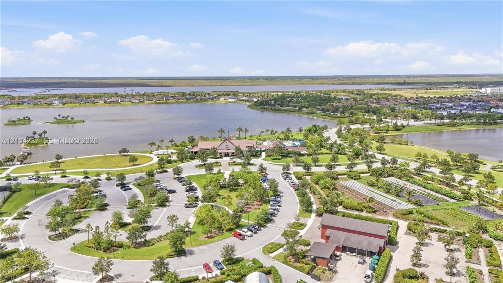 Aerial perspective of a community facility featuring expansive lakefront acreage, manicured green spaces, structured parking areas, and mature landscaping