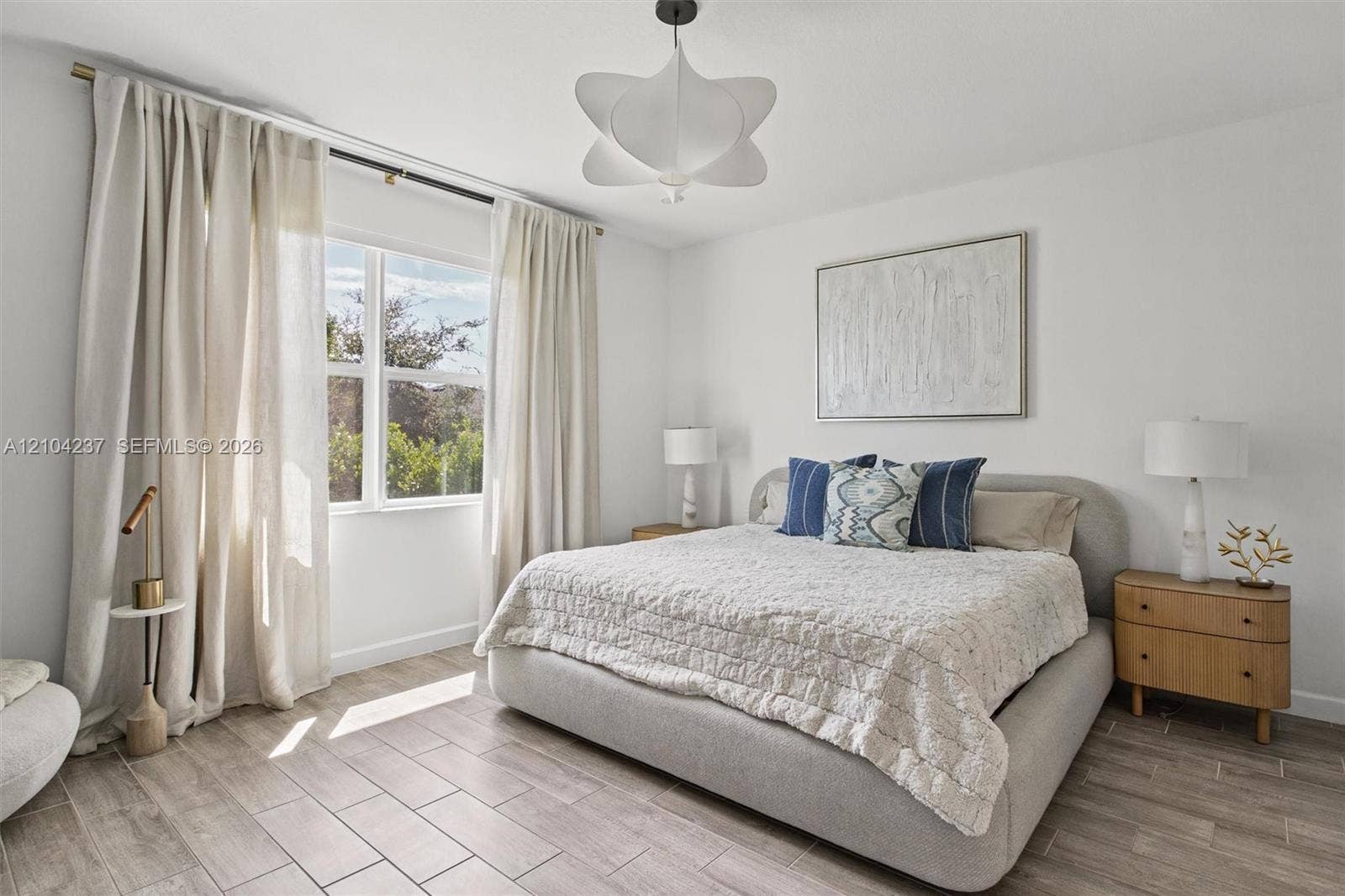 Neutral-toned space featuring wood-finish flooring, a large window with natural light, and a modern sculptural ceiling light fixture