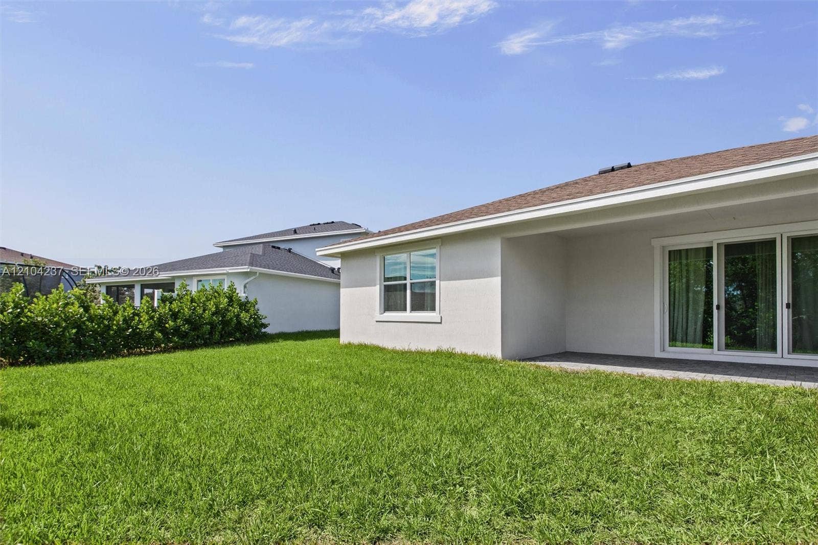 Exterior view featuring a neutral-toned stucco finish, a covered concrete patio, sliding glass doors, and a manicured lawn