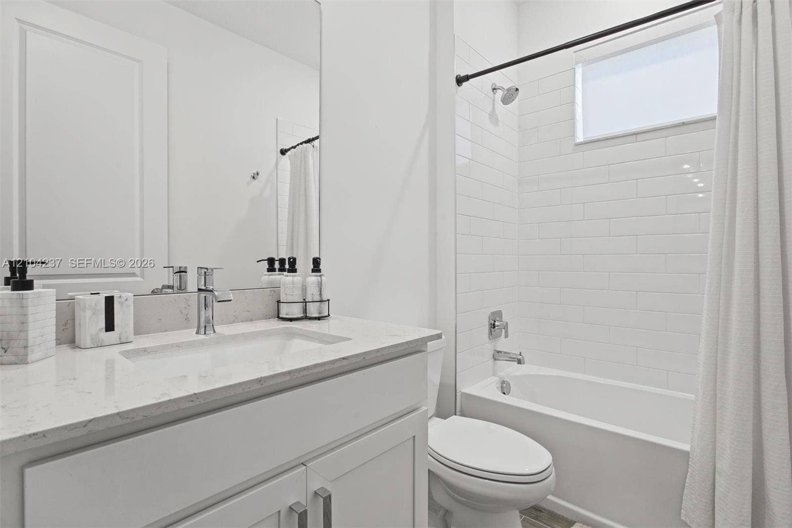 Bathroom featuring a stone-composite countertop, undermount sink, chrome fixtures, white subway tile shower surround, and a clerestory window