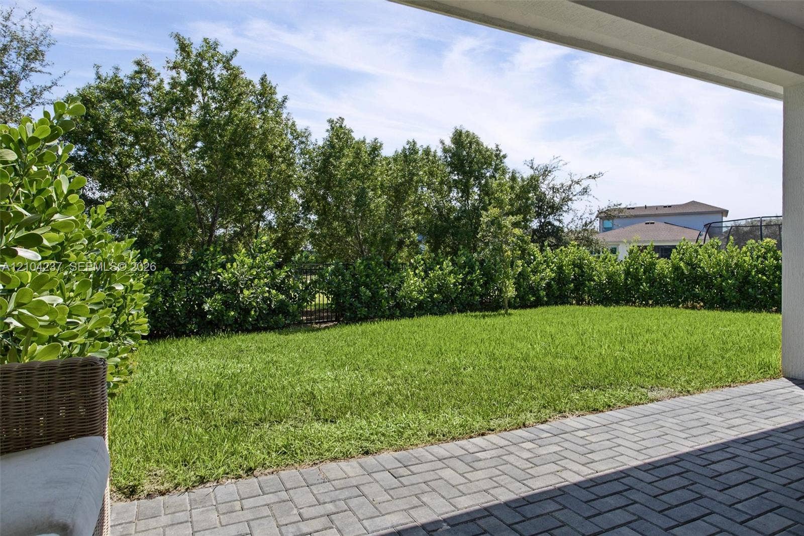 Covered patio featuring paver flooring, overlooking a level lawn enclosed by mature shrubbery and perimeter fencing