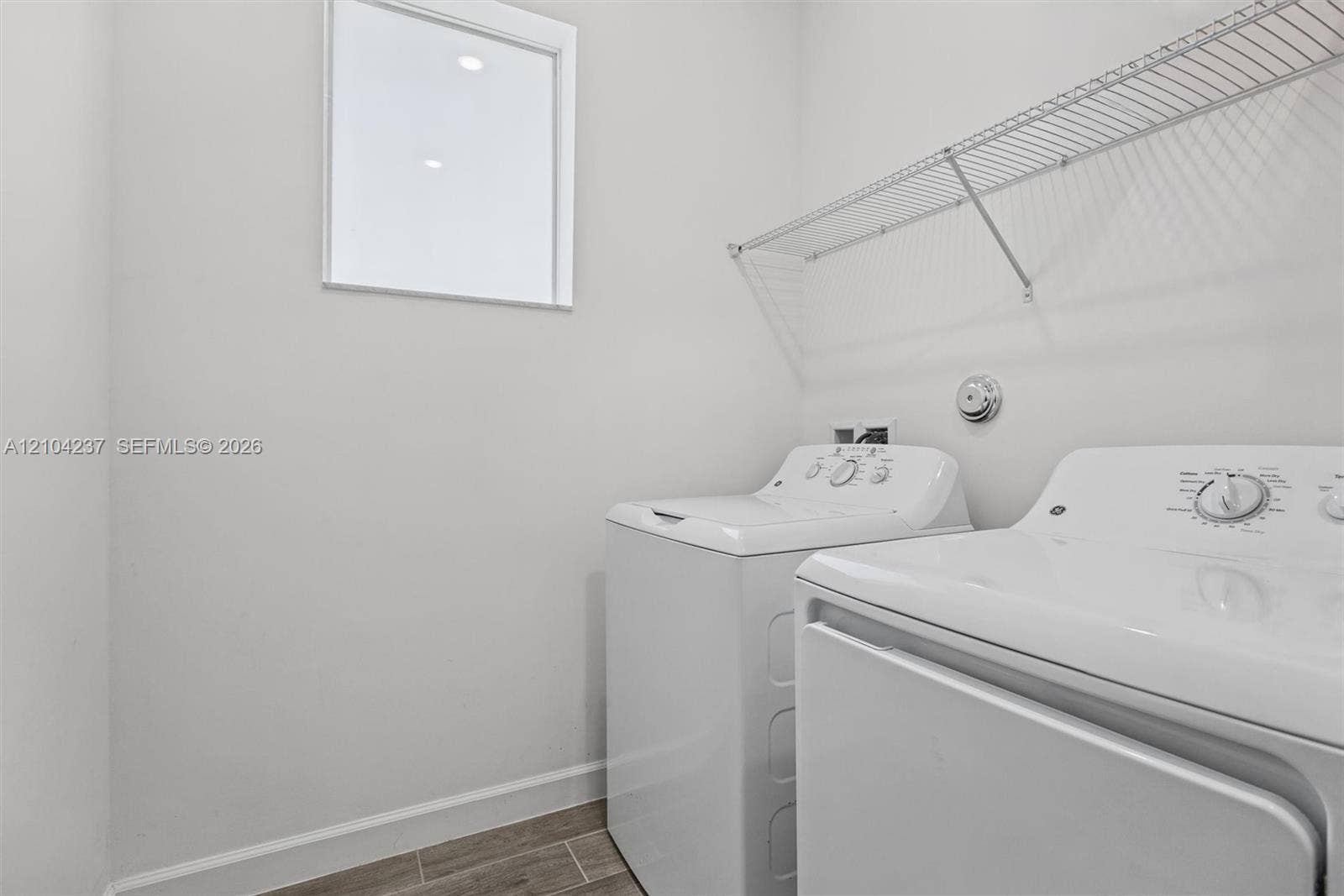 Laundry room featuring wood-finish tile flooring, square window, and wall-mounted wire shelving