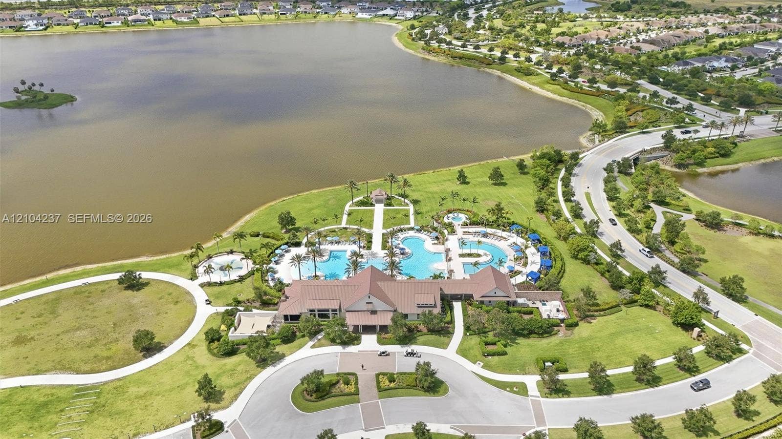 Community amenity center featuring a multi-section swimming pool, paved pedestrian pathways, manicured green space, and lakefront positioning